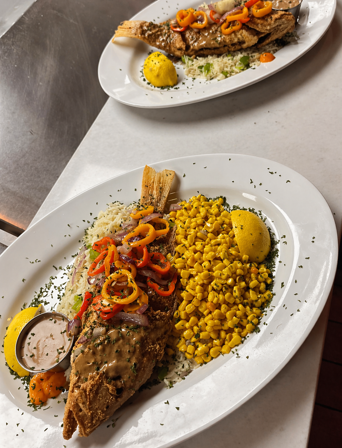 Plates of cooked fish with rice, corn, and vegetables, garnished with lemon wedges and parsley.