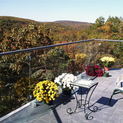 Showcasing a project by DOUBLEPLAY: Balcony with a glass railing with potted chrysanthemums in yellow, white, red, and purple, a small table, a chair, and a view of trees and hills in autumn.