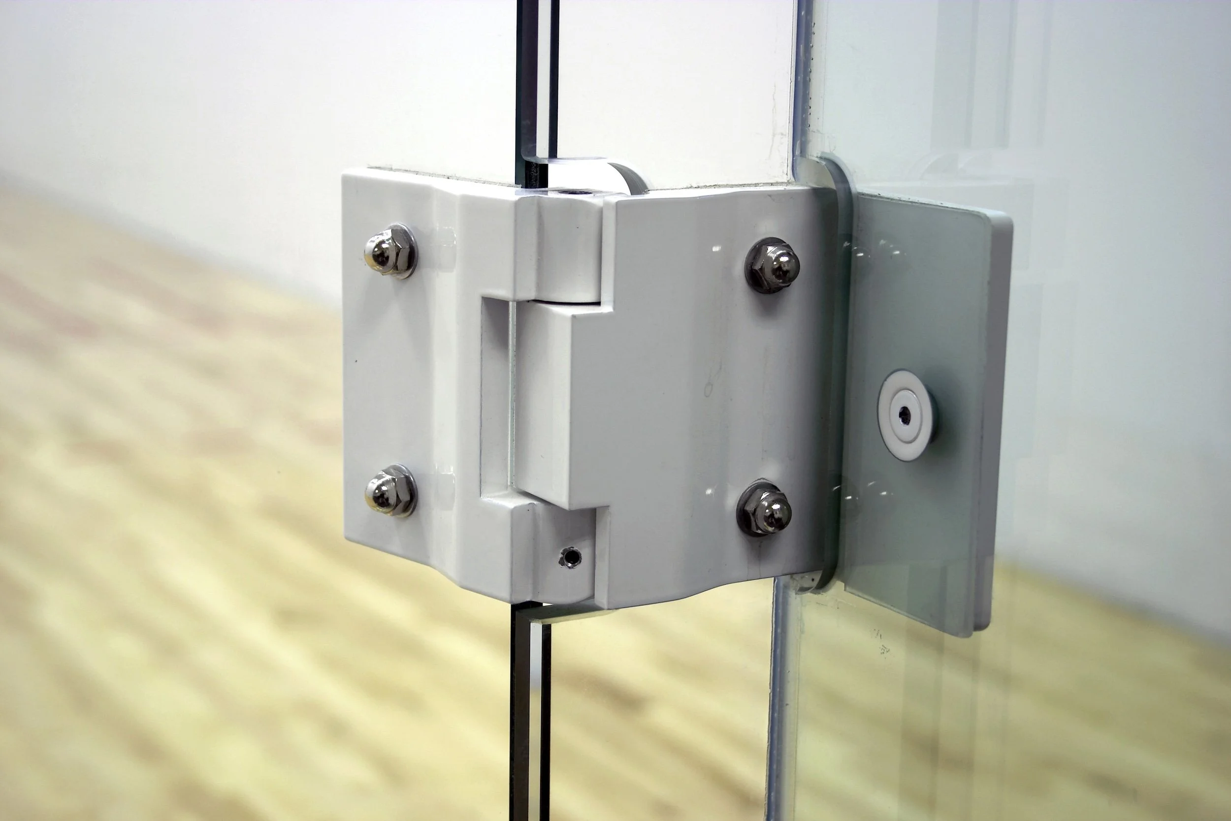Design feature by DOUBLEPLAY: Close-up of a glass door hinge mounted on a white door frame with metal screws