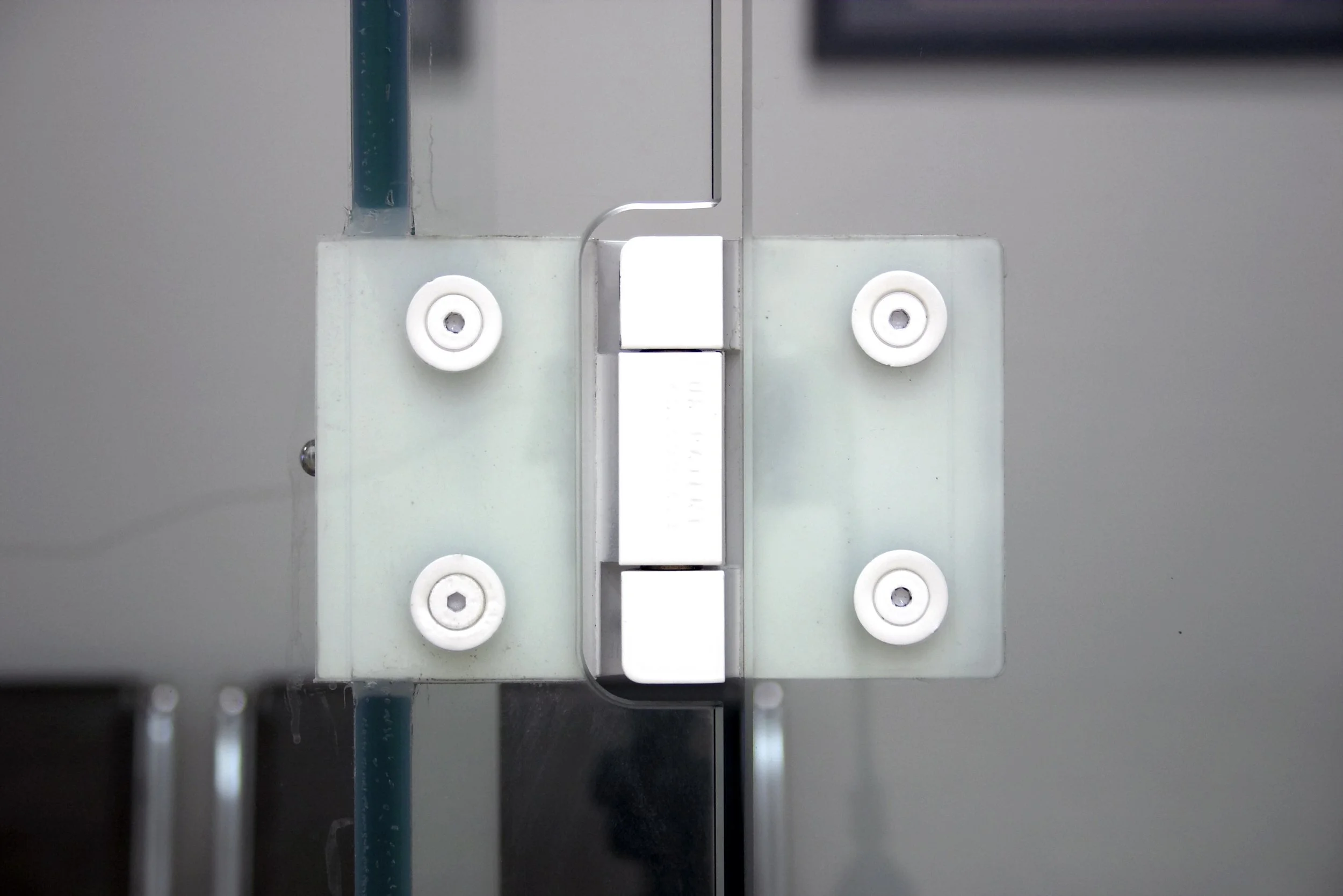 Design feature by DOUBLEPLAY: Close-up of a metallic hinge with four white screws and a white rectangular component, part of a mechanical or electronic device.