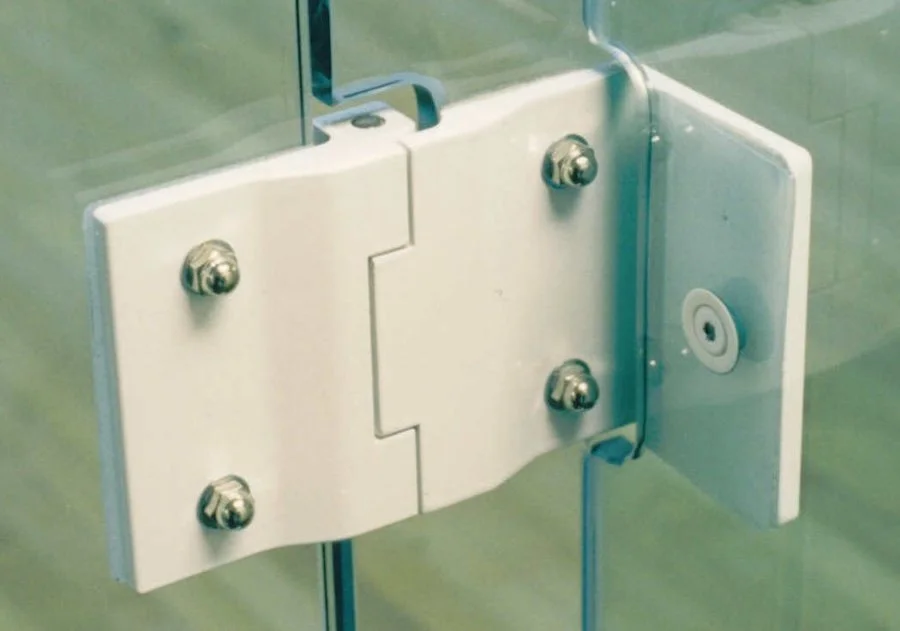 Design feature by DOUBLEPLAY: Close-up image of a glass door hinge with metal screws and a glass door handle mechanism.