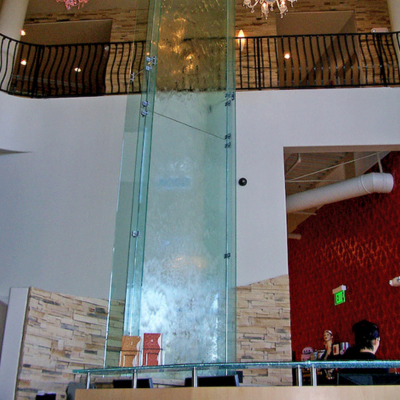 Showcasing a project by DOUBLEPLAY: Indoor water fountain with a glass panel and water cascading down, part of a modern interior design.