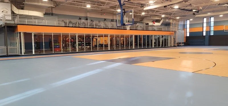 Showcasing a project by DOUBLEPLAY: Indoor basketball court with glass-enclosed fitness or training area on one side.