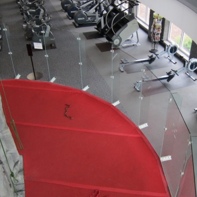 Showcasing a project by DOUBLEPLAY: Indoor gym with exercise equipment and a red, curved railing in the foreground.