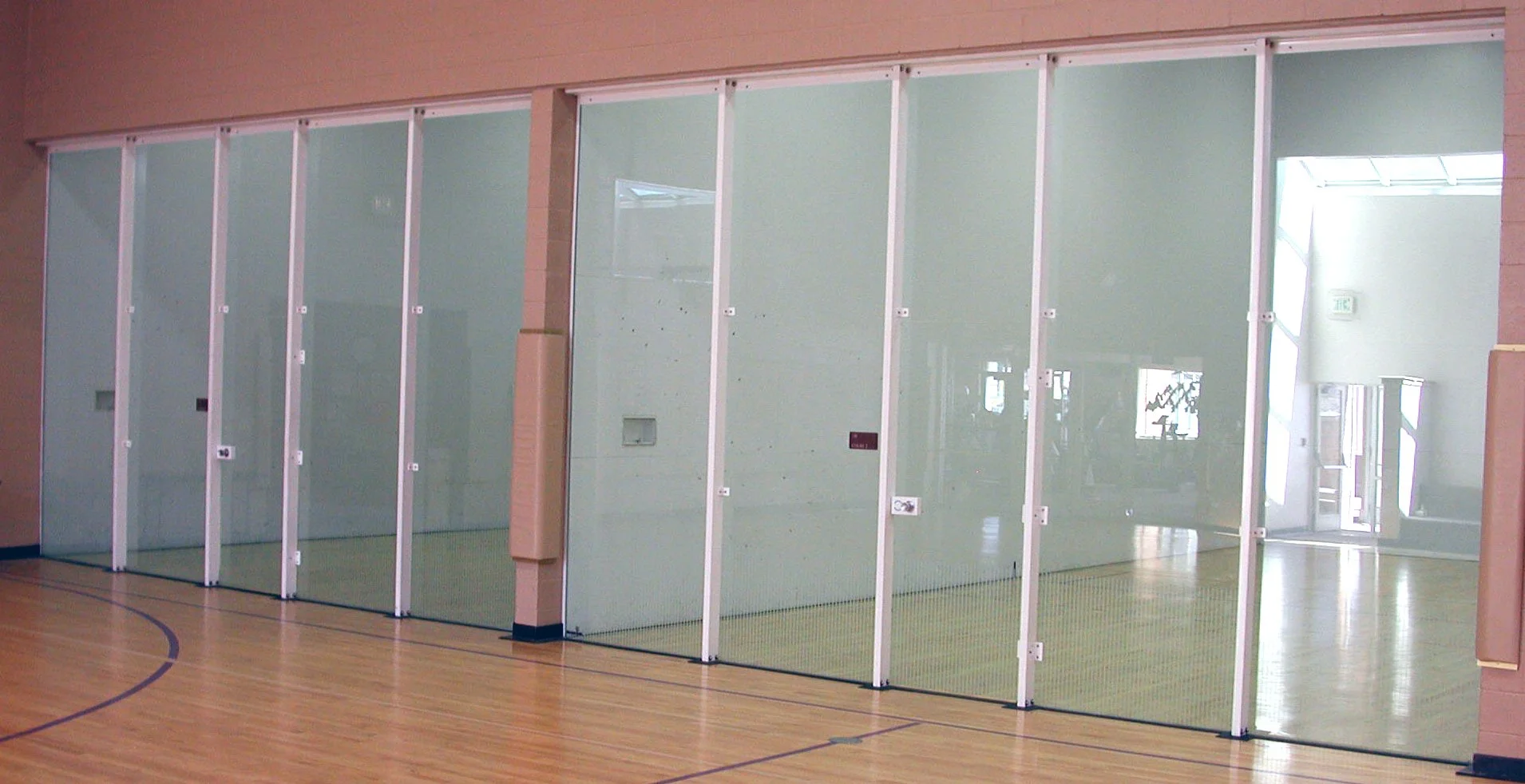 Showcasing a project by DOUBLEPLAY: Indoor sports facility with glass walls and a wooden floor, separated into multiple sections for different activities or classes.