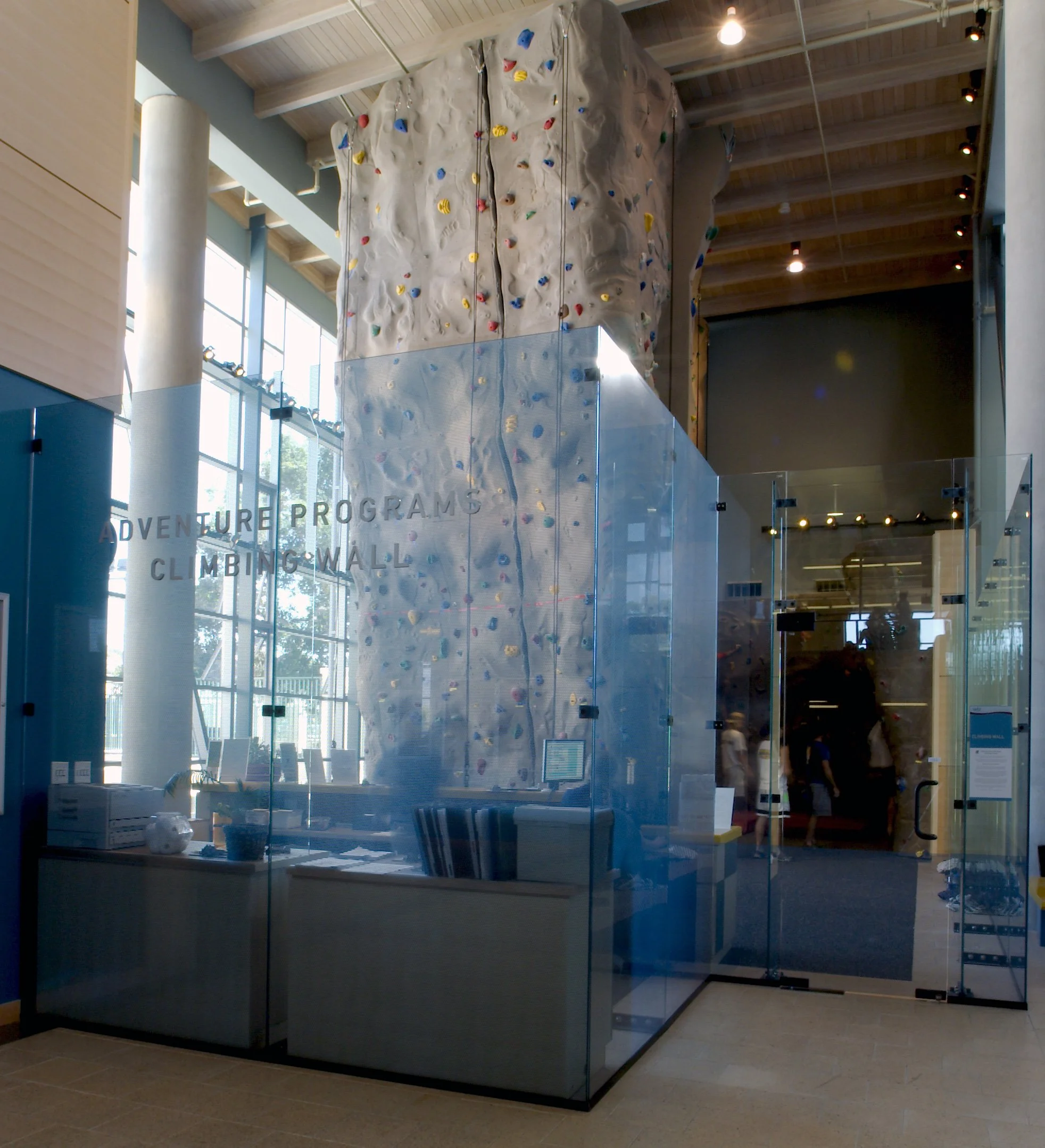 Showcasing a project by DOUBLEPLAY: Indoor rock climbing wall with colorful holds, enclosed in a glass case, with a high ceiling and large windows in the background.