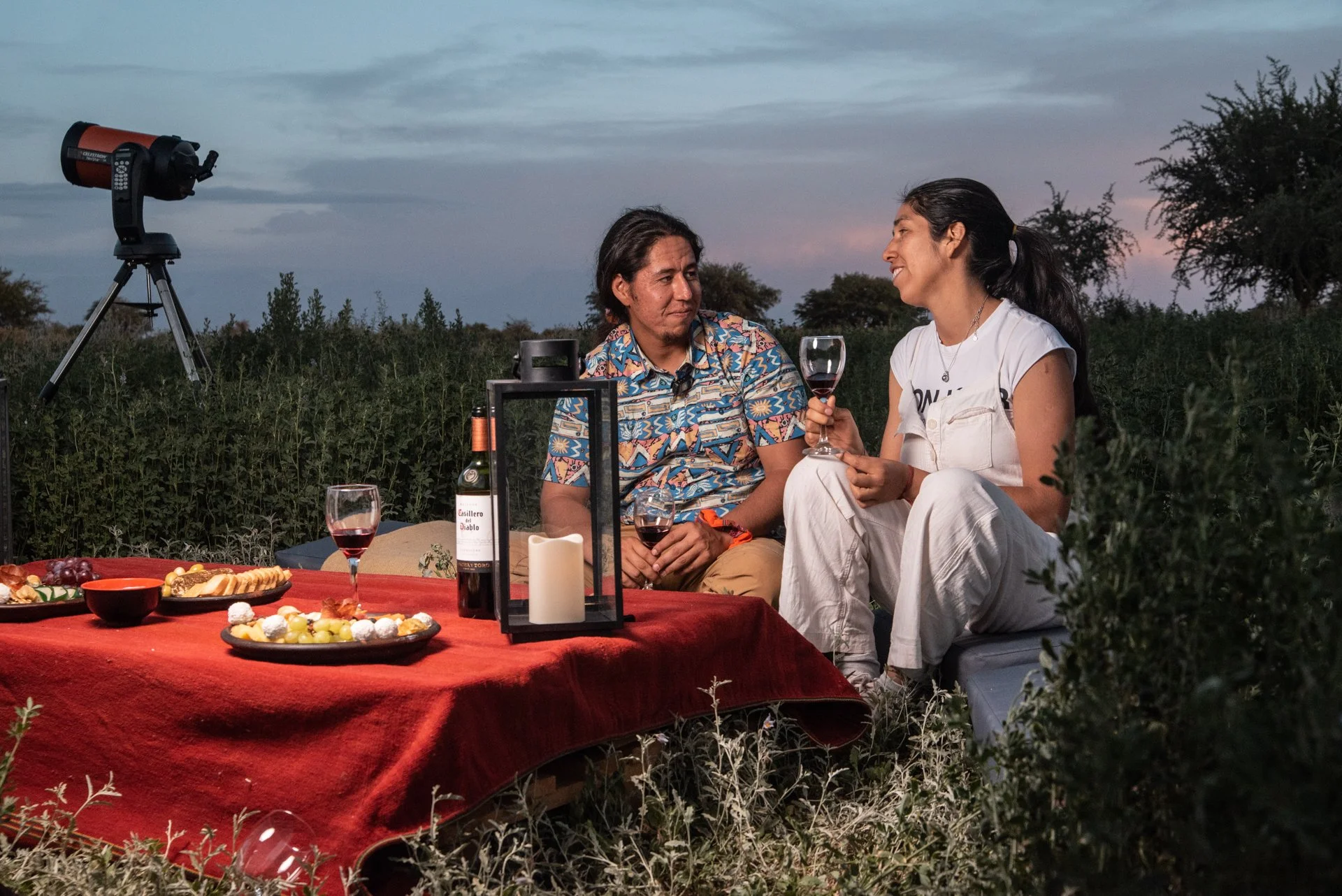 Couple enjoying wine during an outdoor stargazing tour in San Pedro de Atacama with a telescope set up in the background.