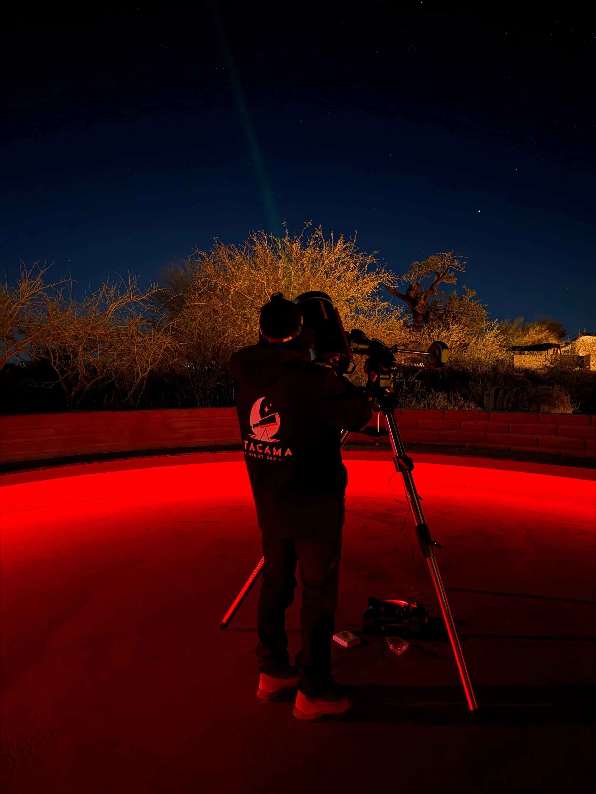 Astronomy guide in an Atacama Night Sky jacket adjusting a professional telescope inside a red-lit stargazing observatory ring at night.