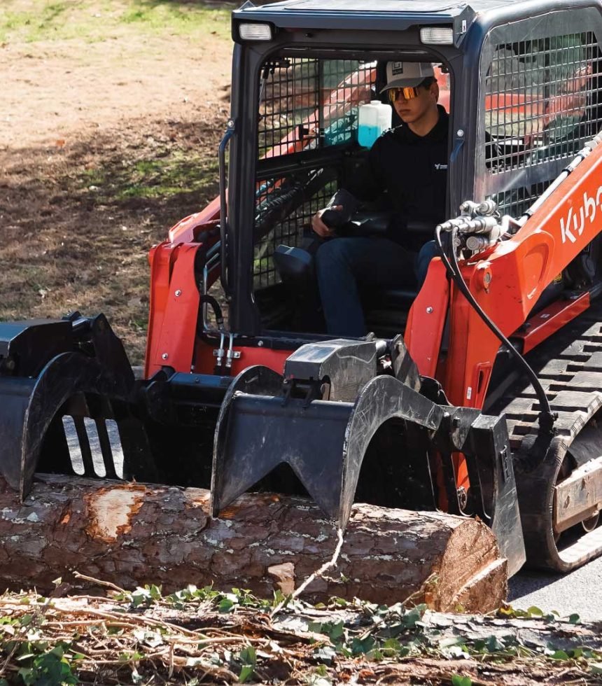 Timber Tree Services operator using a Kubota skid-steer loader with a log grapple attachment for commercial tree removal and land clearing
