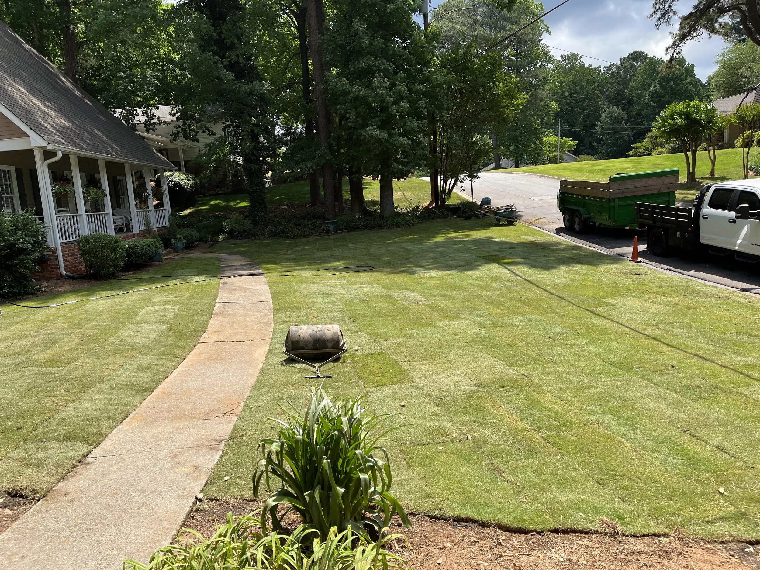 Timber Tree Services crew completing a residential landscape installation with equipment and trailer at a home with a manicured front yard