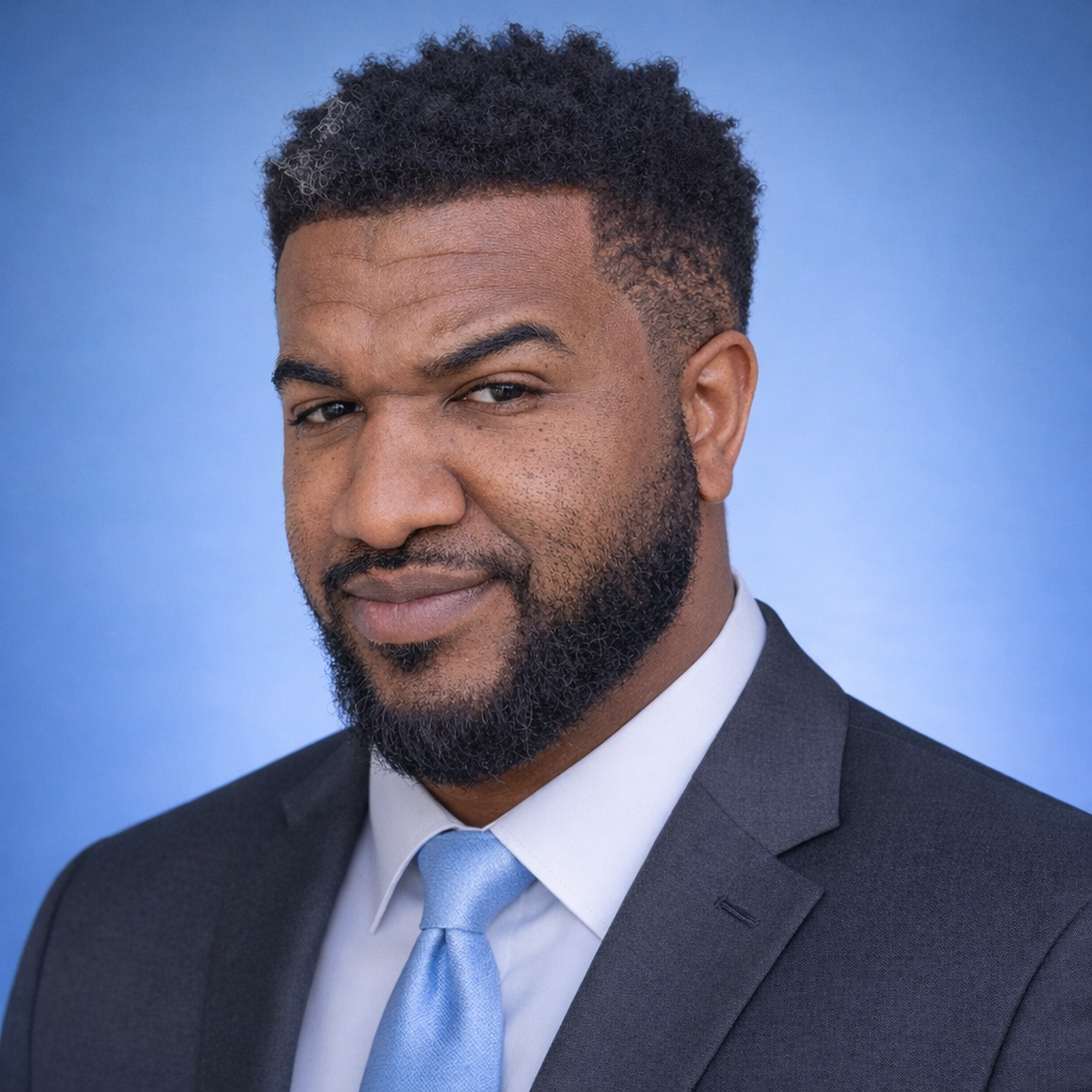 A professional man with a beard and short, curly hair, dressed in a dark suit and light blue tie, against a blue background.