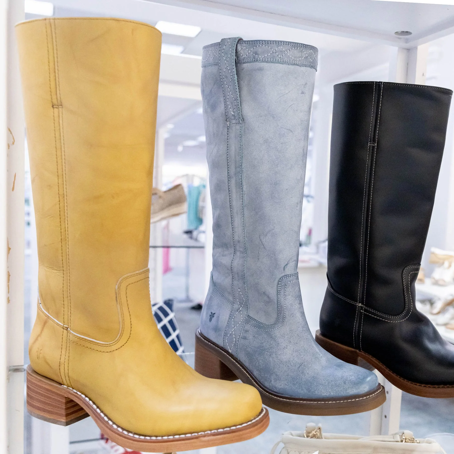 Three knee-high boots in yellow, light blue, and black displayed on a shelf.