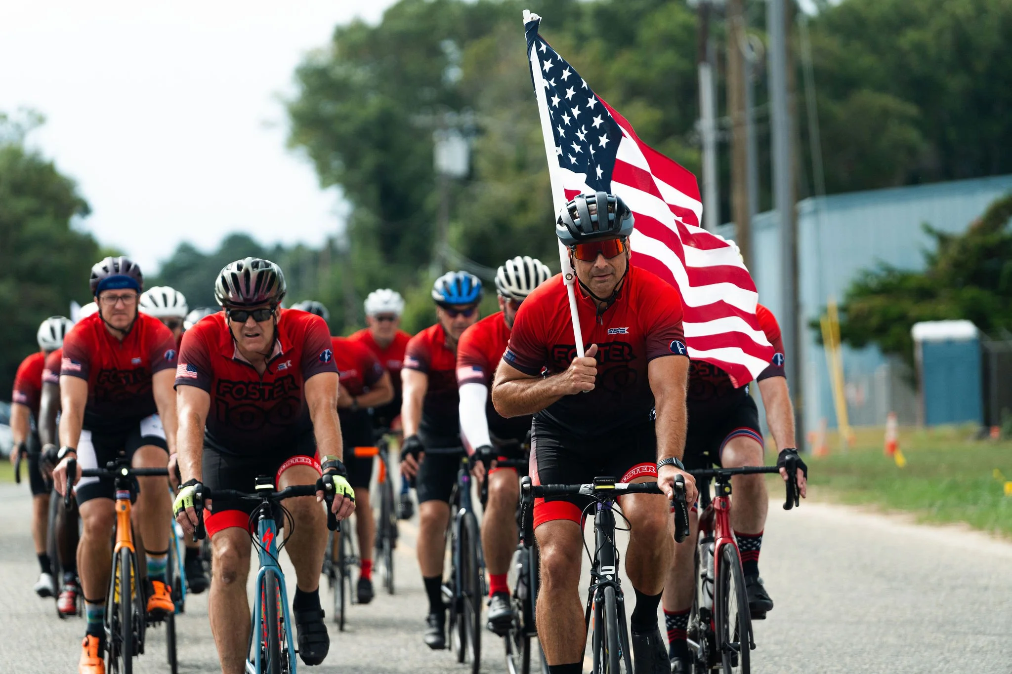 A group of men riding bicycles in a race, with one man at the front holding an American flag.