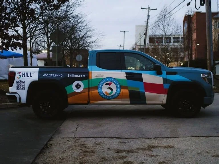 A pickup truck with a colorful wrap promoting Three Hill Craft Beer. The wrap features the company's logo, contact information, and a multicolored design.