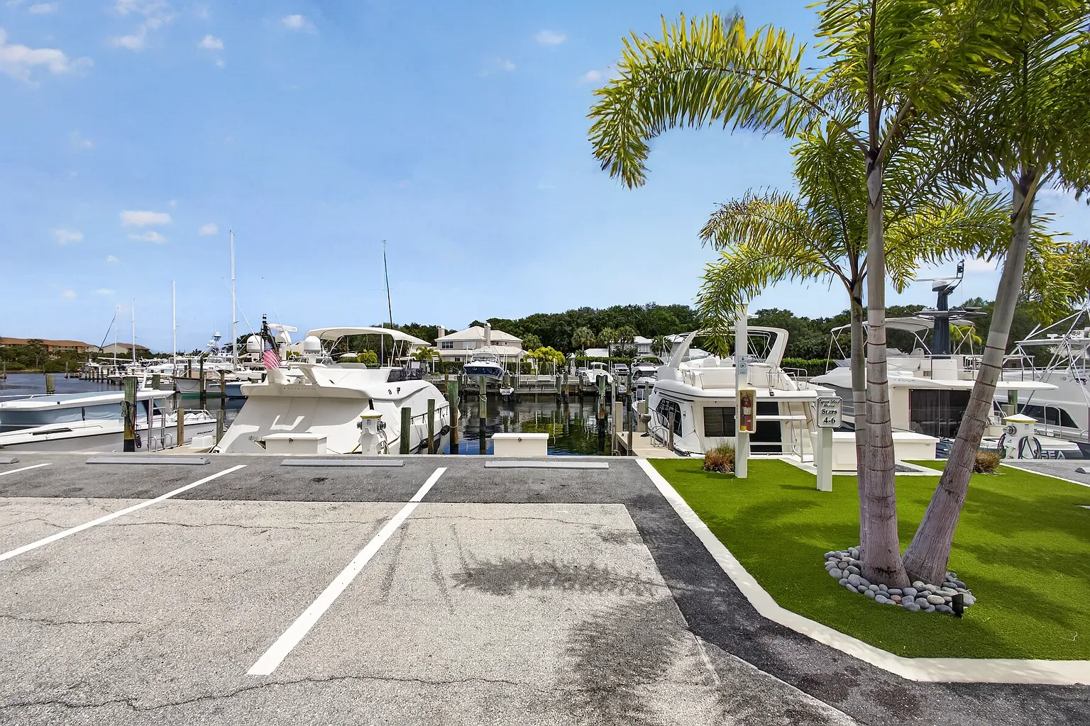 Marina with boats docked, palm trees, and parking lot in the foreground on a clear day.