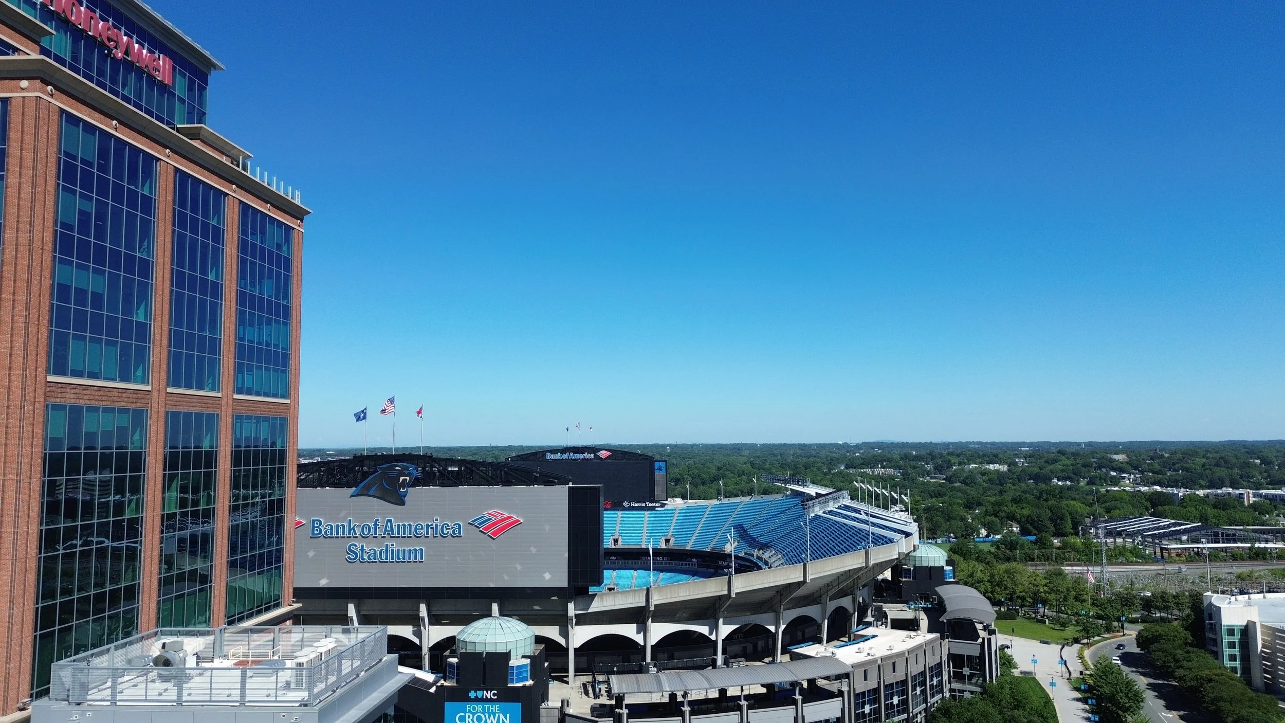 A view of Bank of America Stadium, home of the Carolina Panthers, with a tall glass building on the left and a clear blue sky overhead.