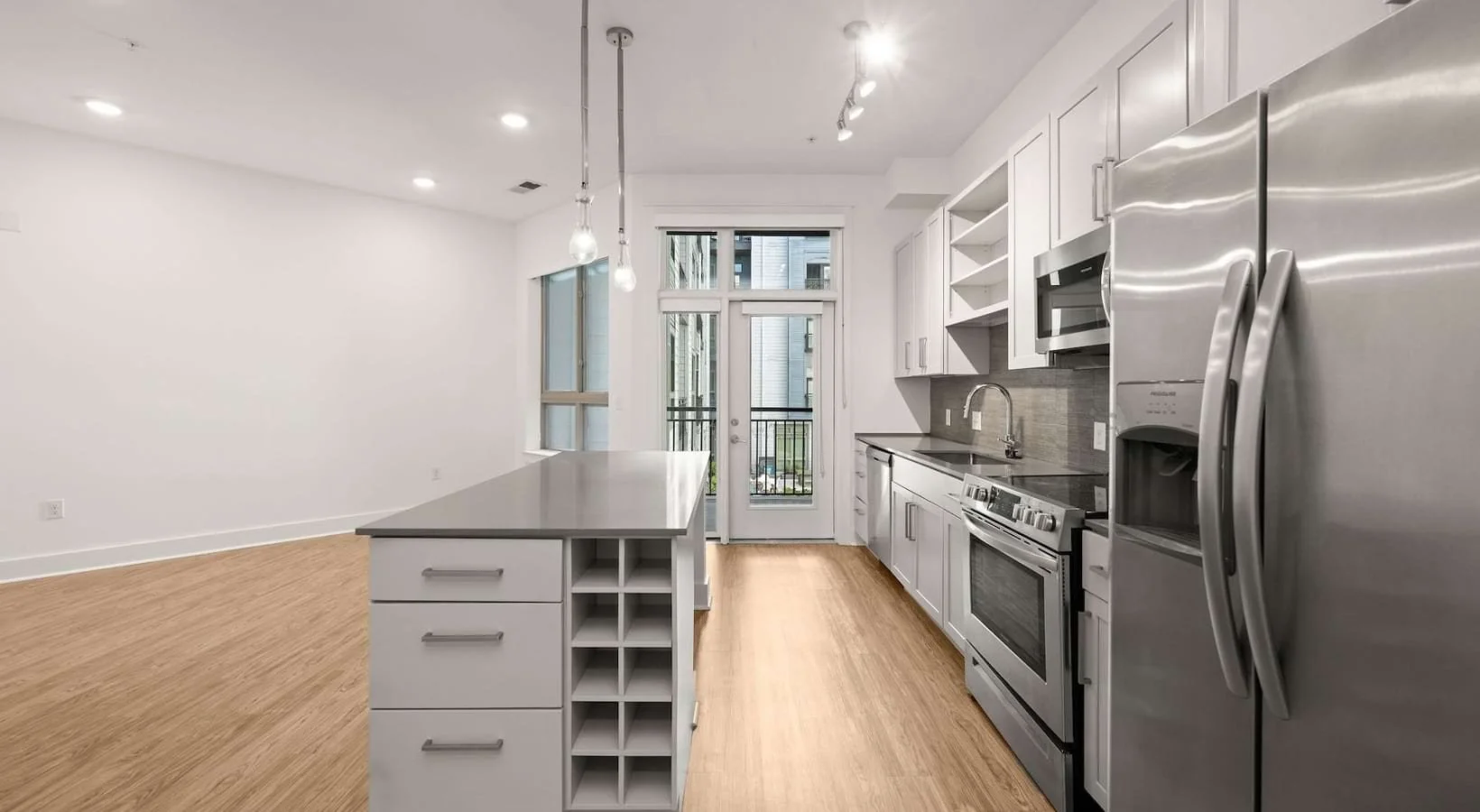 Modern kitchen with white cabinetry, stainless steel appliances, a kitchen island, and hardwood floors in an apartment setting.