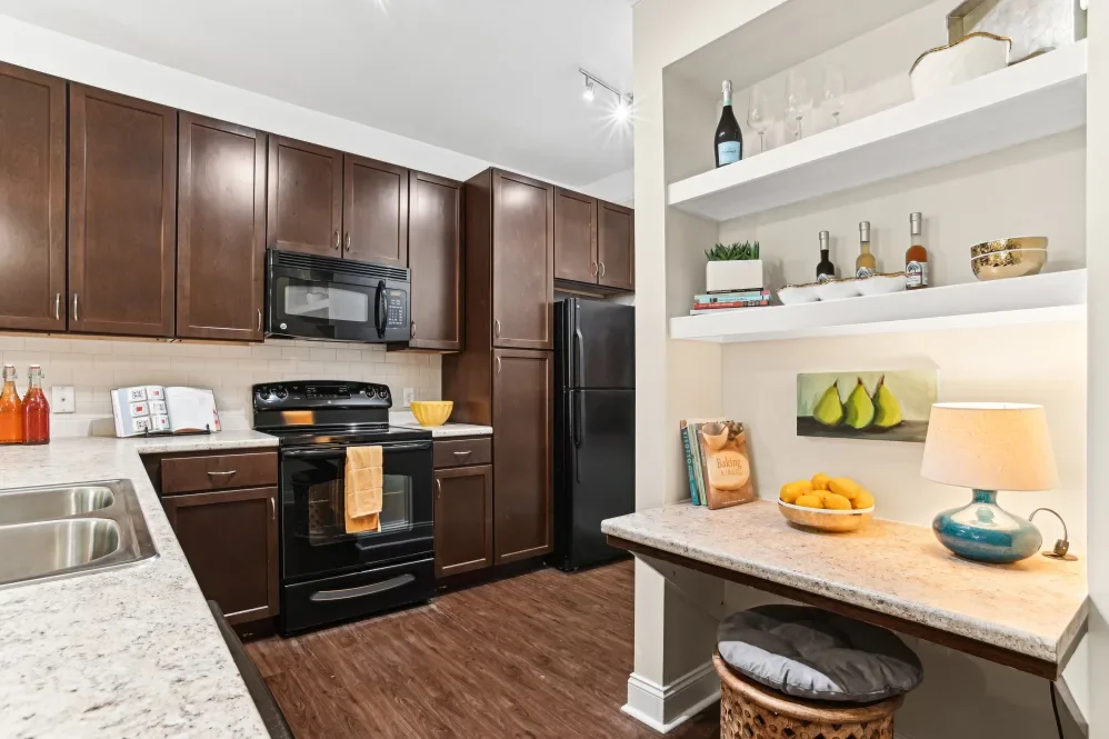 Kitchen with dark wooden cabinets, black appliances, white countertops, and open shelves with decorative items, books, and a bowl of lemons.