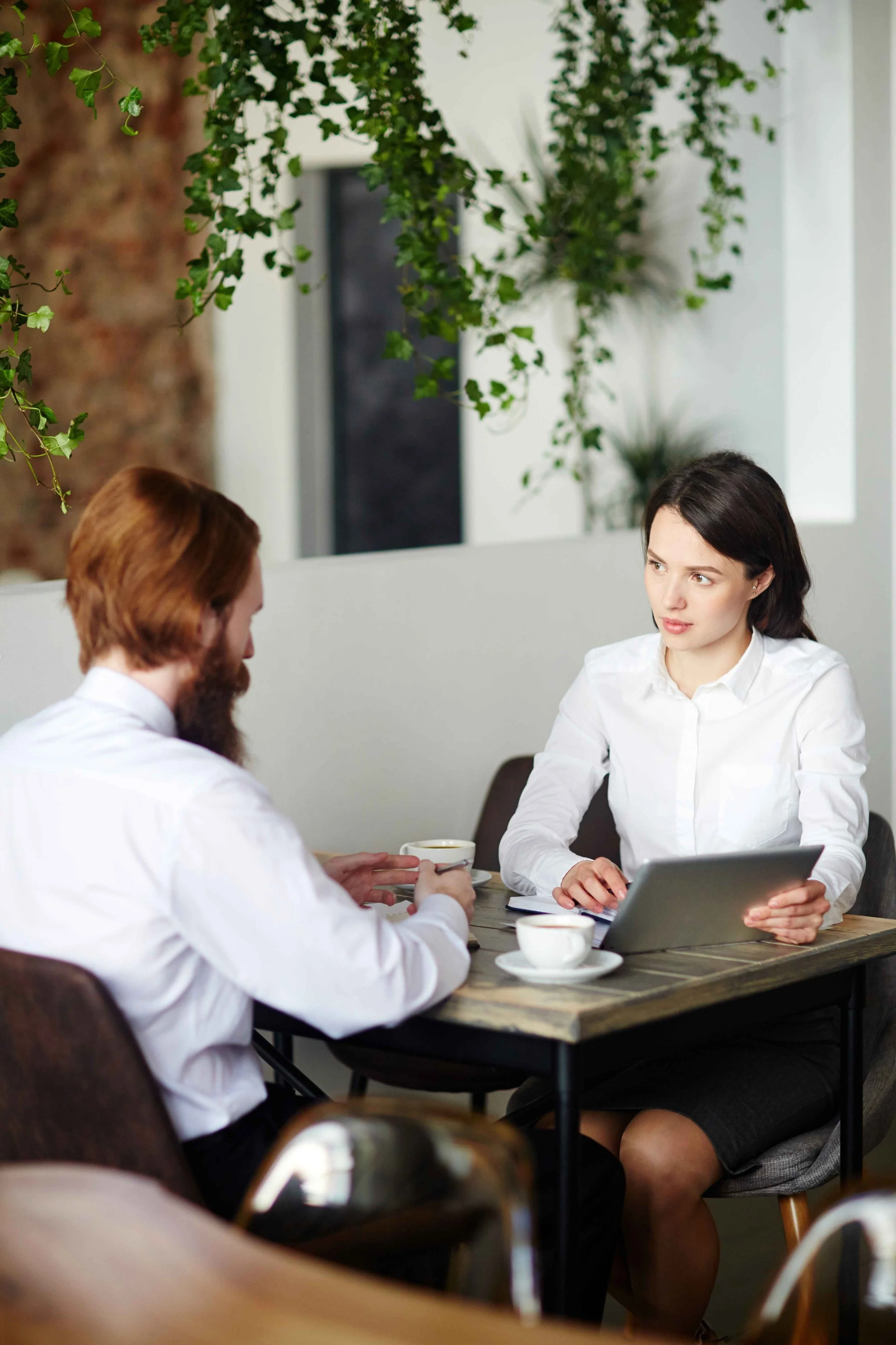 Young Registered Associate Nutritionist wearing smart clothes listening to client in cafe, holding tablet ready to take notes