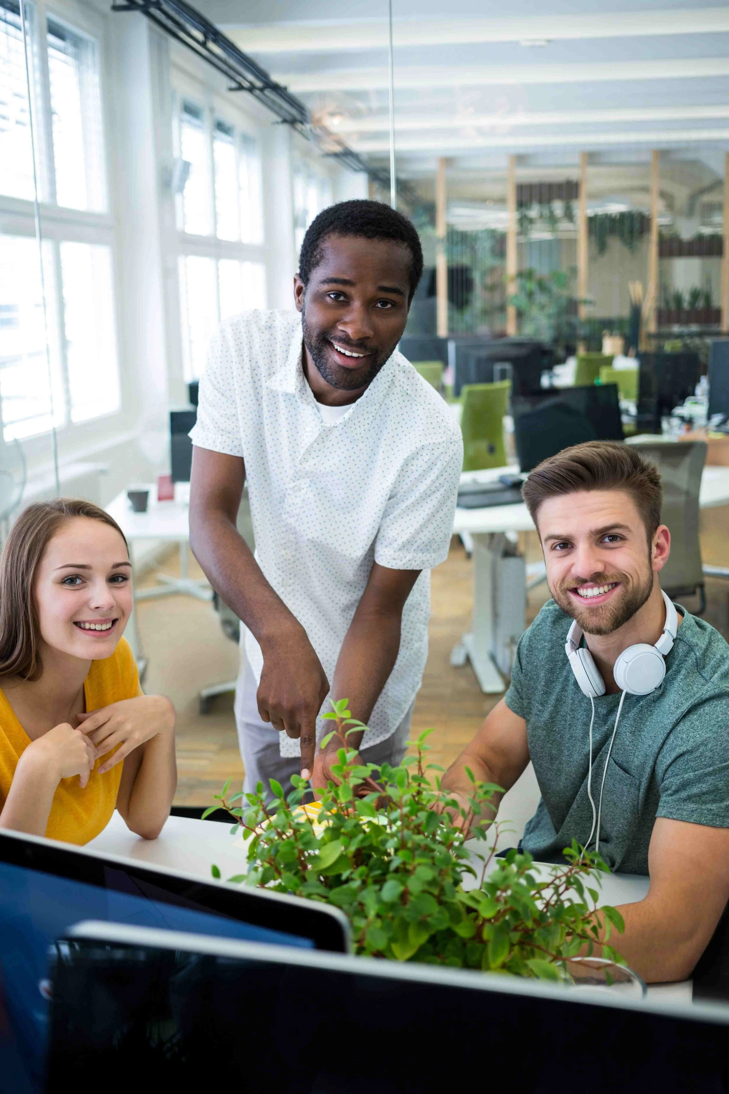 Three young office workers smiling at desk with a plant on the table