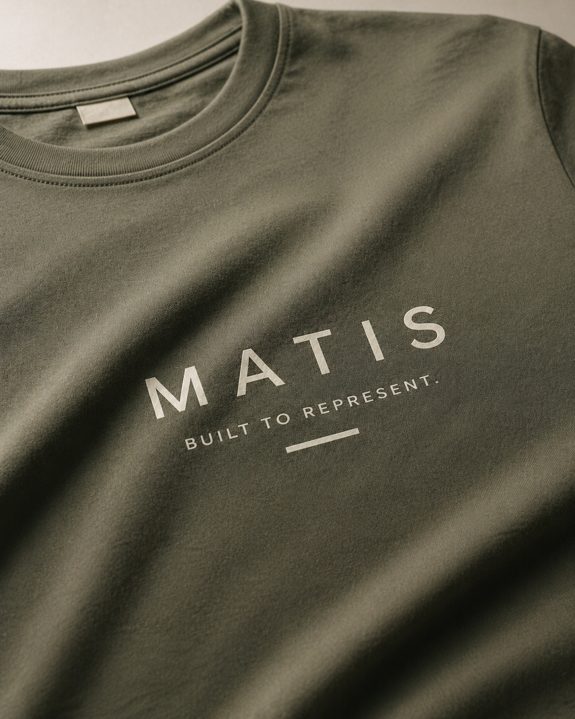 Grünes T-Shirt mit weißem Druck, der die Marke 'MATIS' und den Satz 'BUILT TO REPRESENT' zeigt.