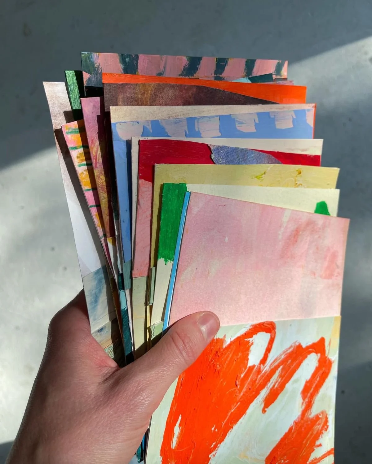 Hand holding a fan of colorful abstract paintings or drawings on paper.