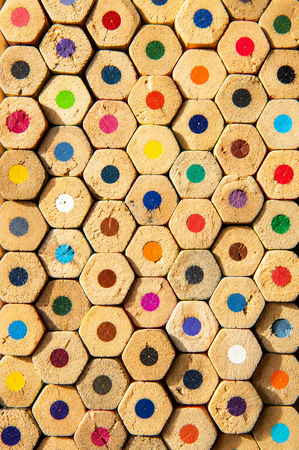 Close-up of a large collection of sharpened colored pencils with hexagonal tips, arranged with colored dots on the ends.