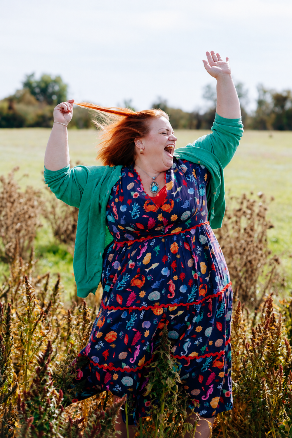 Jodie laughing in a field, arms up, hair flying