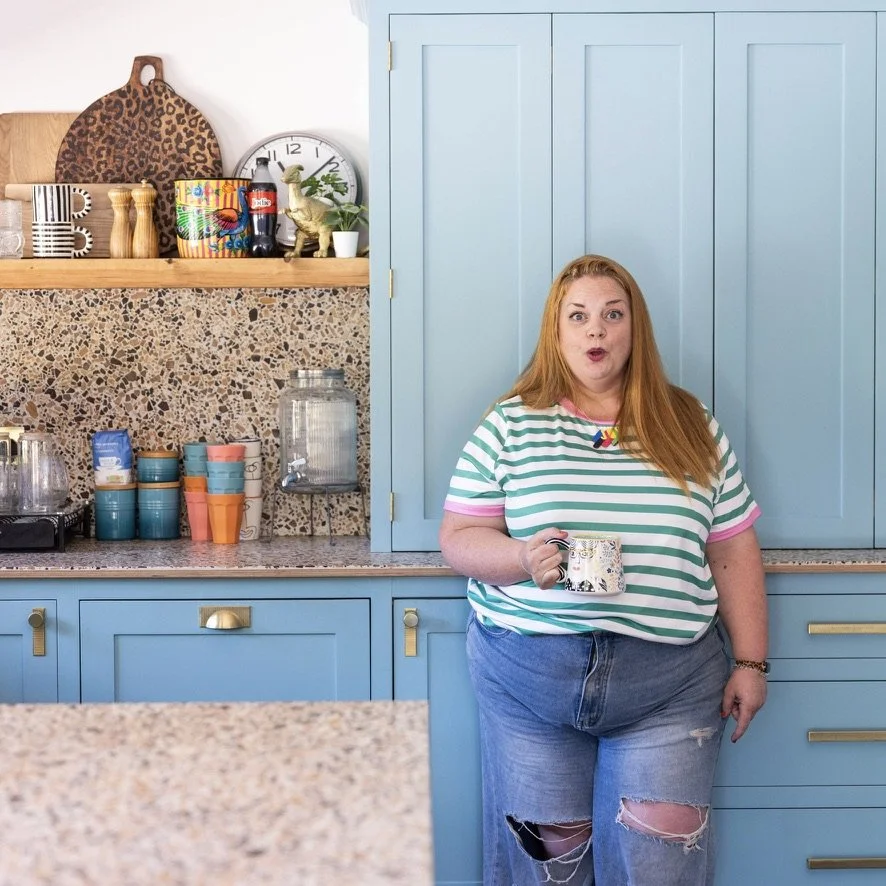 Jodie in her kitchen in a green striped t-shirt, holding a mug and looking surprised