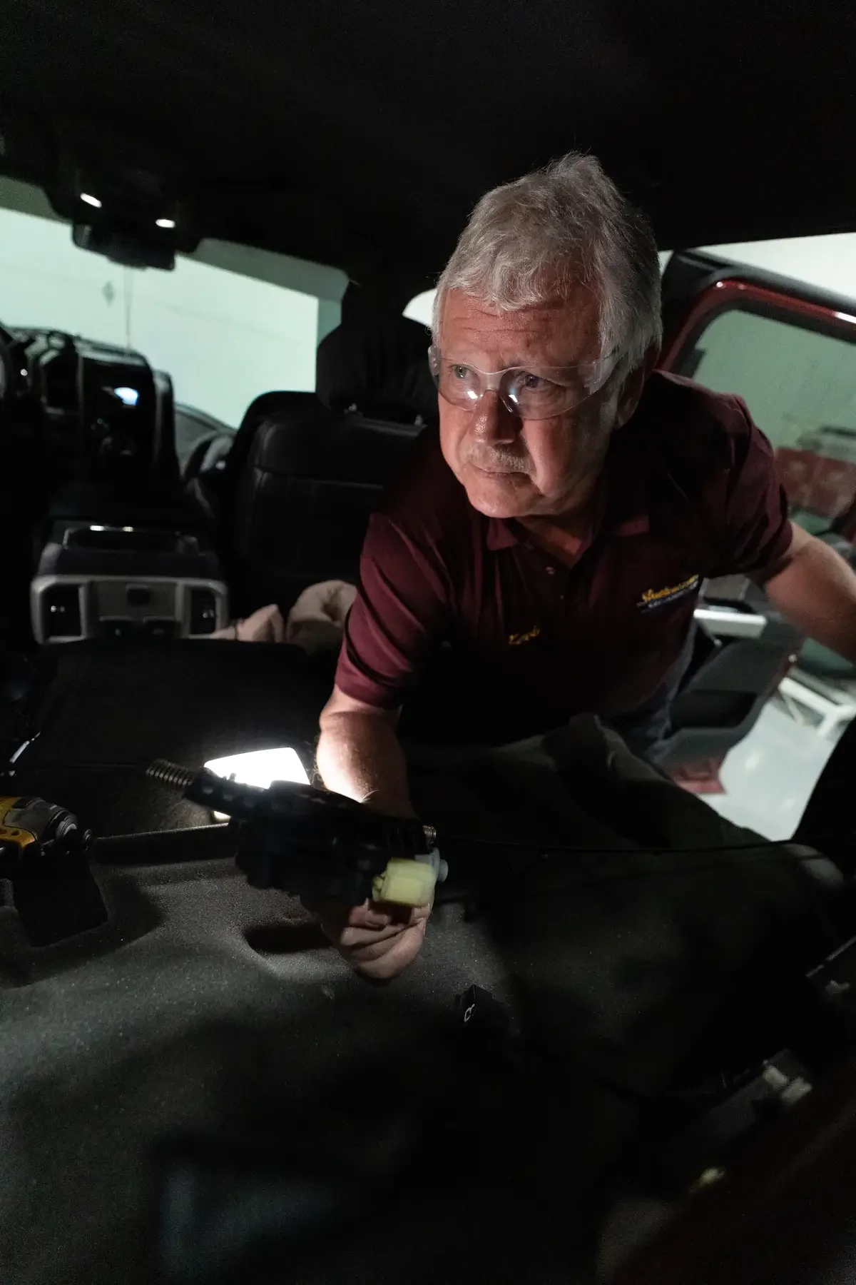 Kevin working inside a vehicle's trunk or cargo area, holding a yellow and black tool or device.