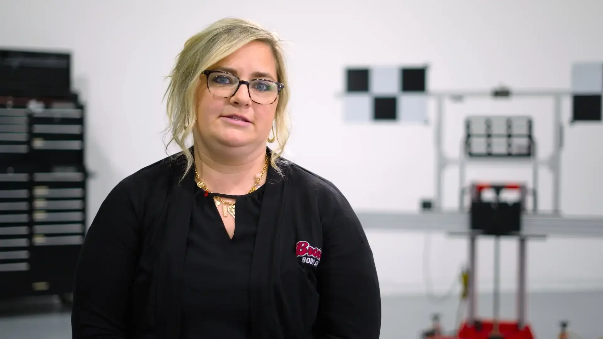 A woman with blonde hair, wearing glasses and a black shirt, sitting at Southeastern Glass Co giving a testimony.