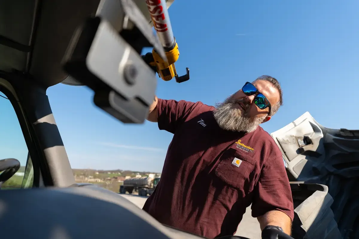 Tim performing glass repair on a vehicle outdoors on a sunny day.
