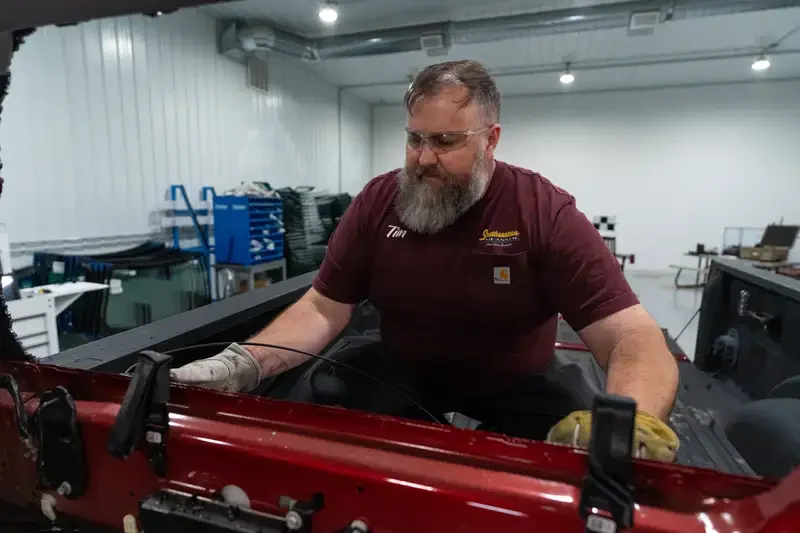 Tim working on a red vehicle in a glass repair workshop.