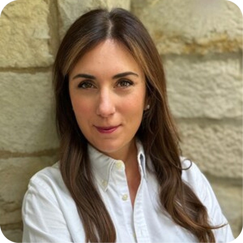 A woman with long brown hair and a white shirt standing against a stone wall.