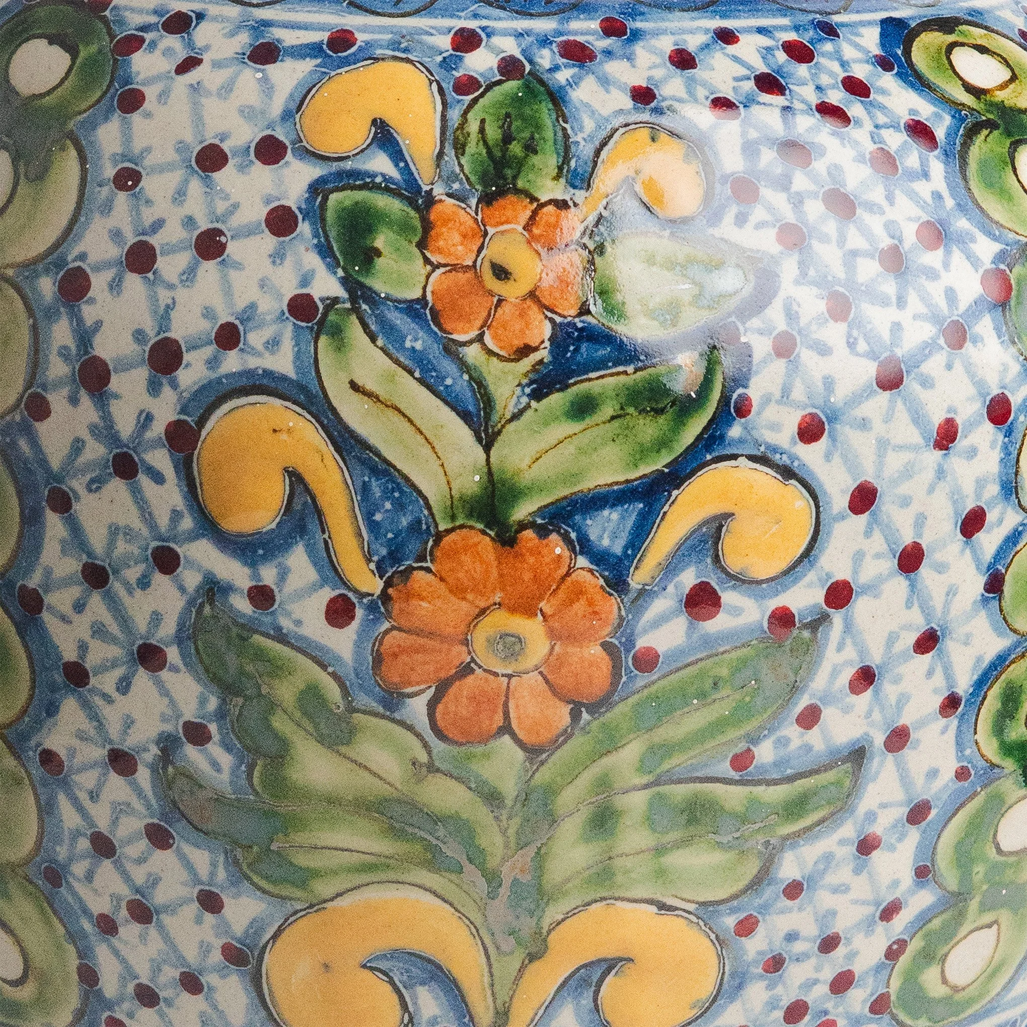 Cuadro pintado con acuarela que presenta flores coloridas y frutas como aguacate, limón y naranja, con fondo azul y detalles en rojo y verde.