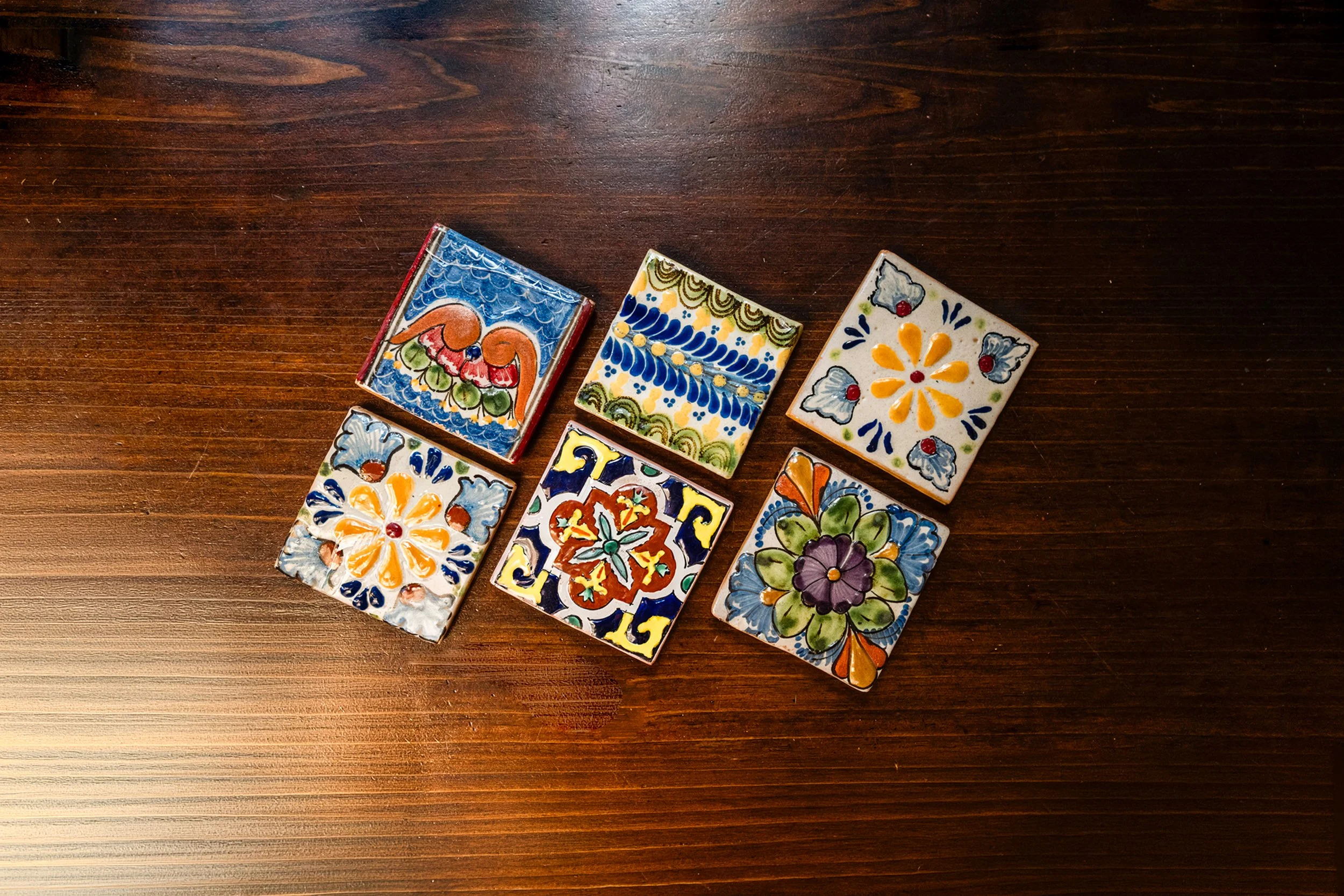 Azulejos de talavera cerámica artesanal decorados con patrones florales y geométricos, dispuestos en una mesa de madera.