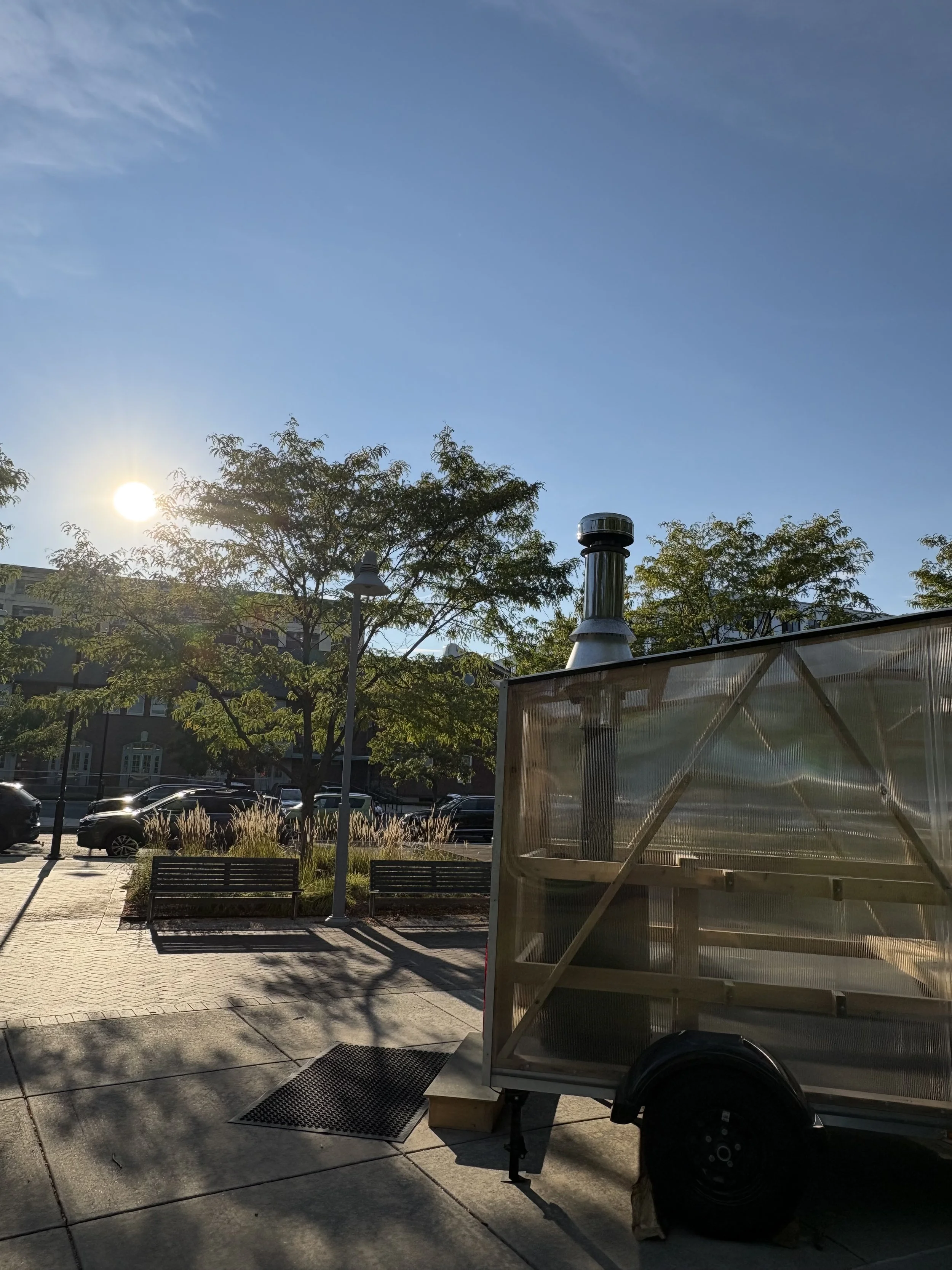 Image of a portable wood-fired sauna parked in front of an office complex for a corporate event.