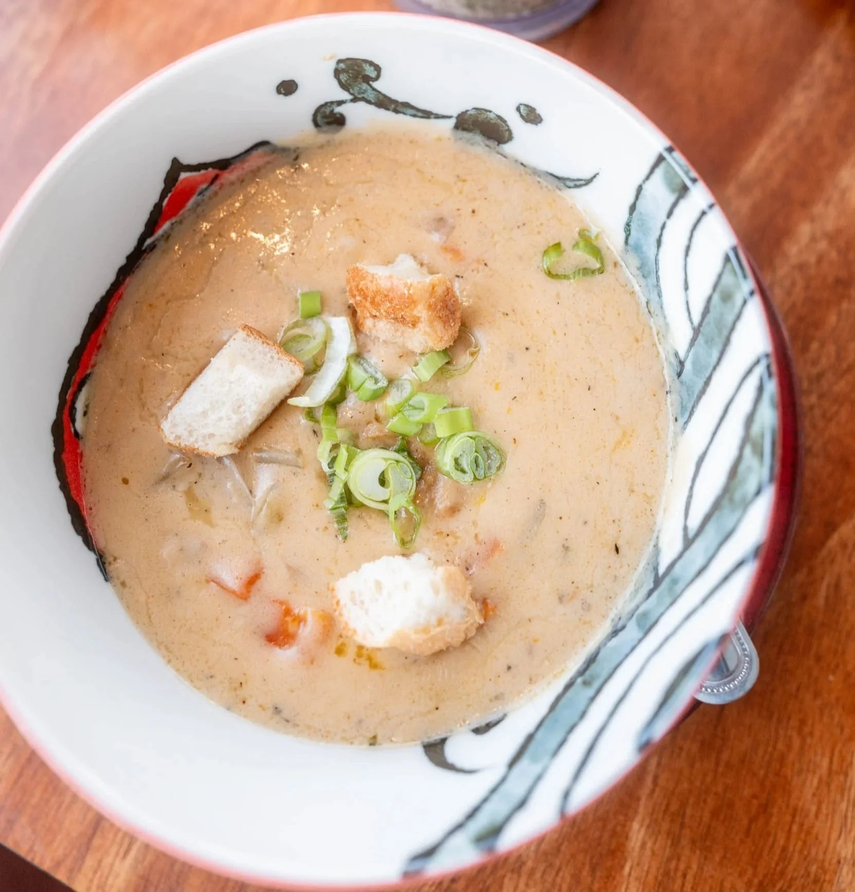Bowl of creamy soup with green onions and croutons, placed on a wooden surface.
