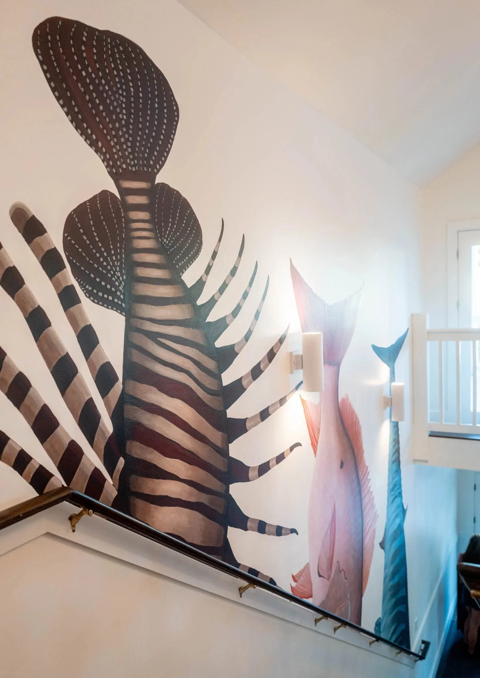 A mural of a zebra with outstretched legs on a wall, near a hallway staircase and a window with closed blinds.