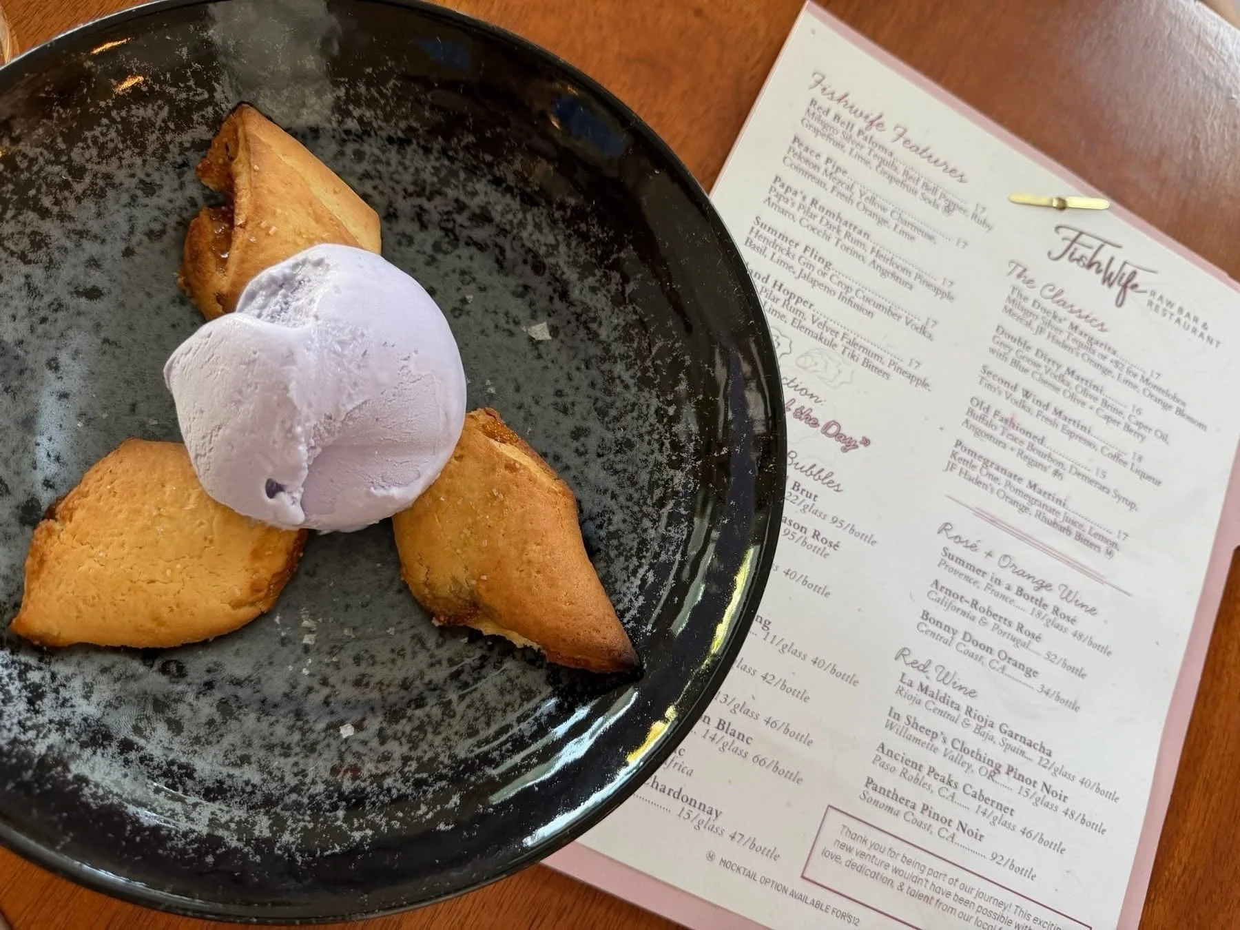 A black plate with four fried triangled empanadas, topped with a dollop of white cream or sauce, on a wooden table.