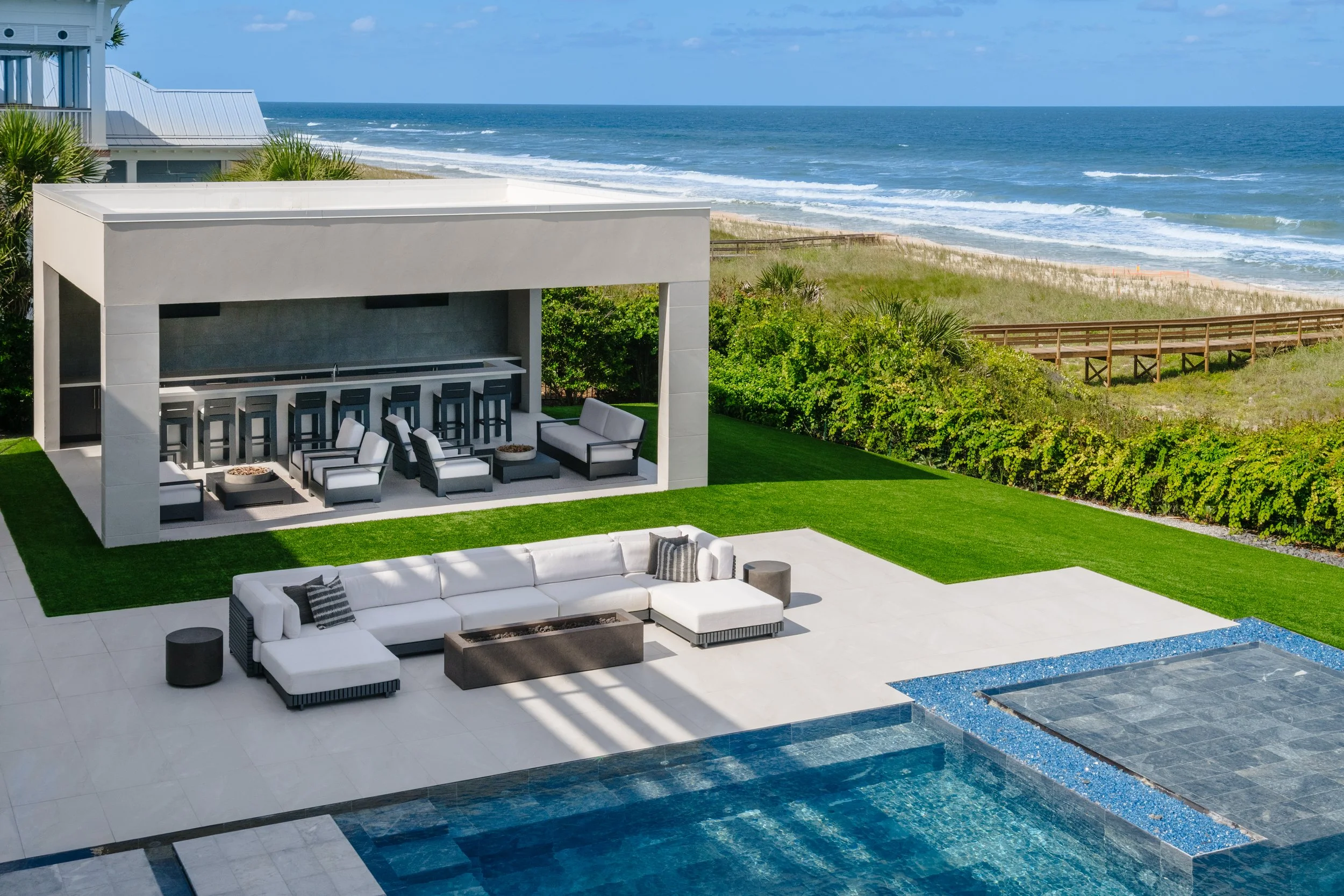 Modern outdoor patio with white and black furniture overlooking the beach and ocean with blue sky.
