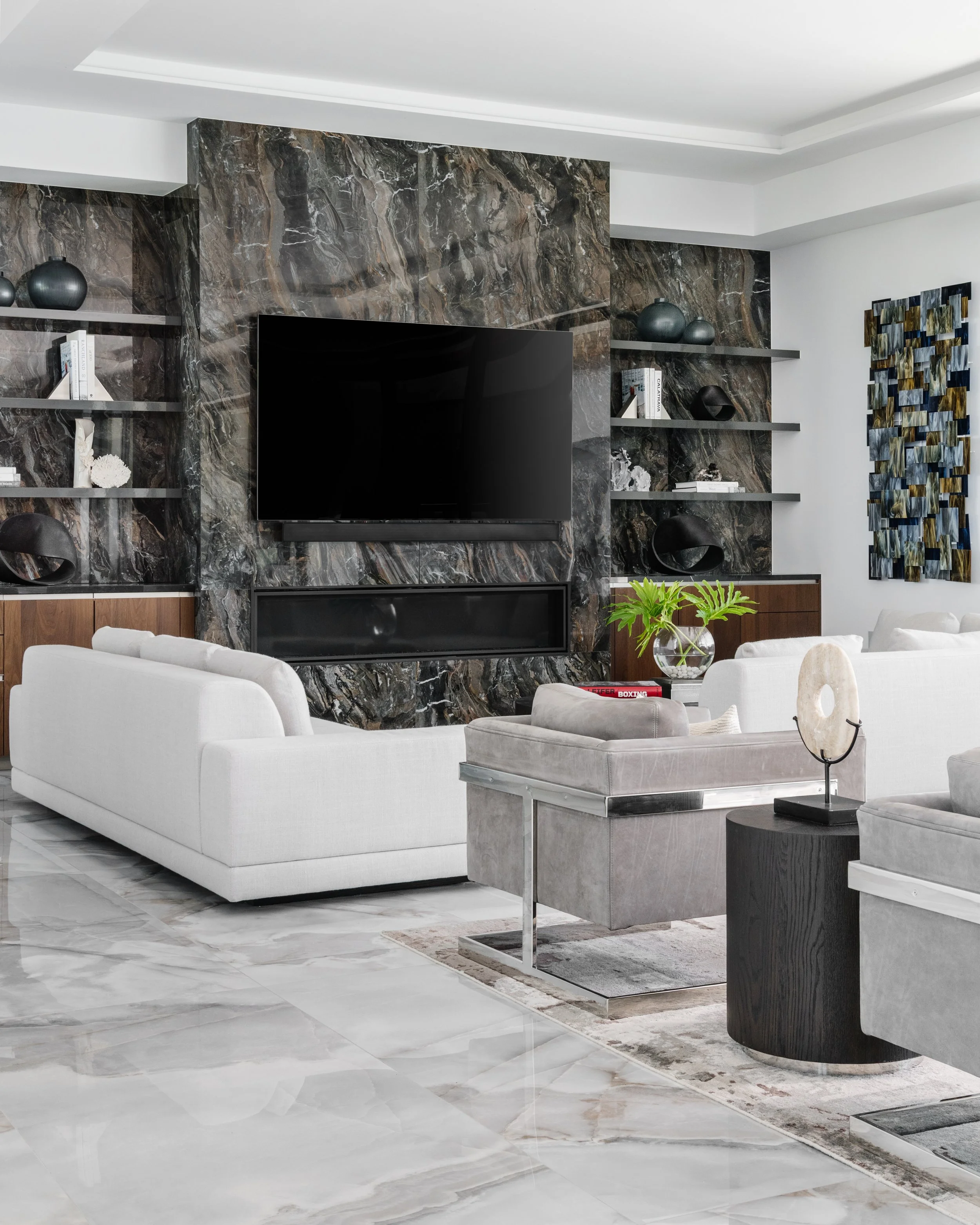 Living room with white sofa, gray marble and black wood furniture, black TV, decorative vases, shelves with books and decor, abstract wall art, and marble flooring.