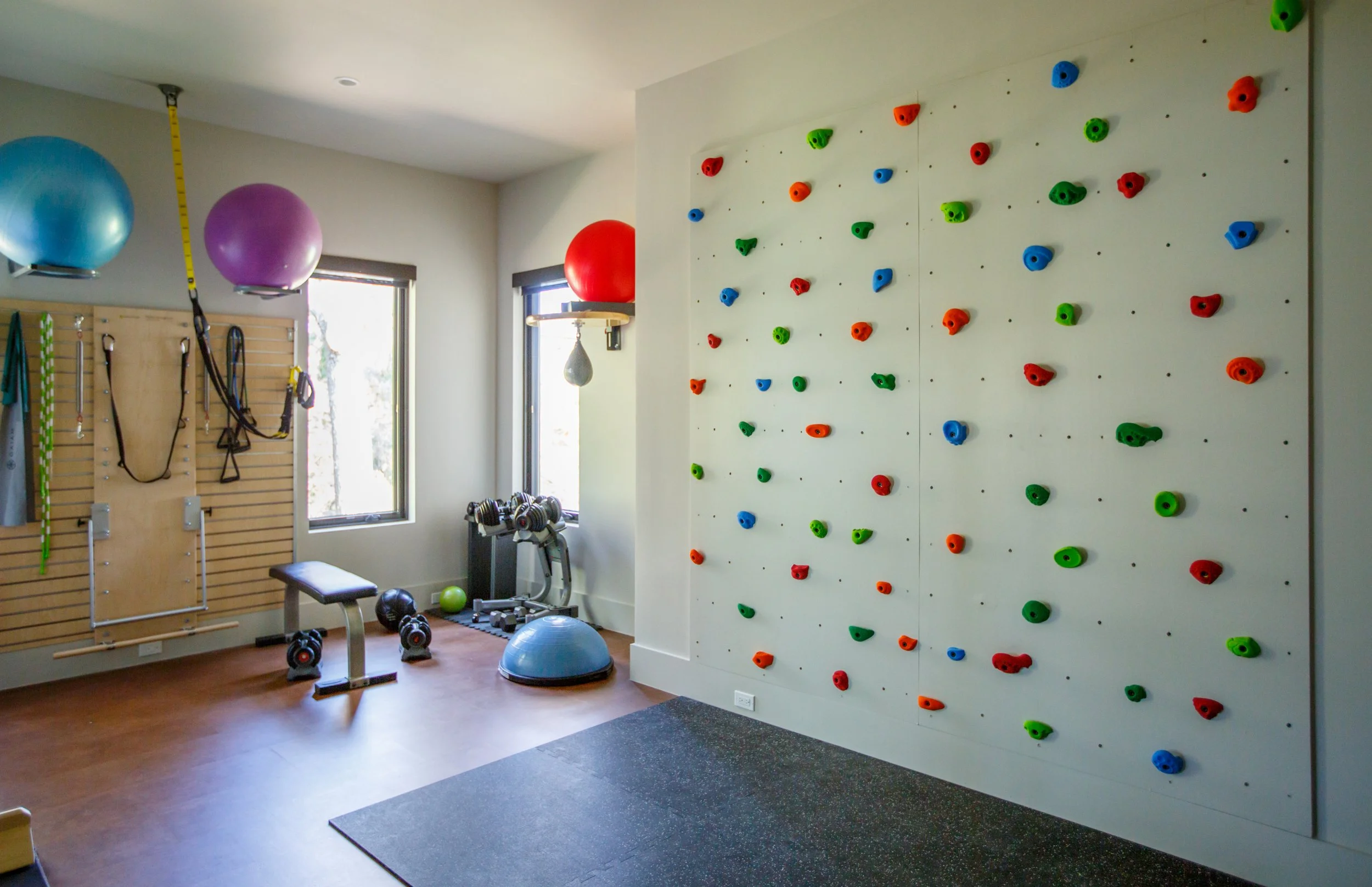 Home gym with a rock climbing wall, exercise balls, dumbbells, kettlebells, and a bench.