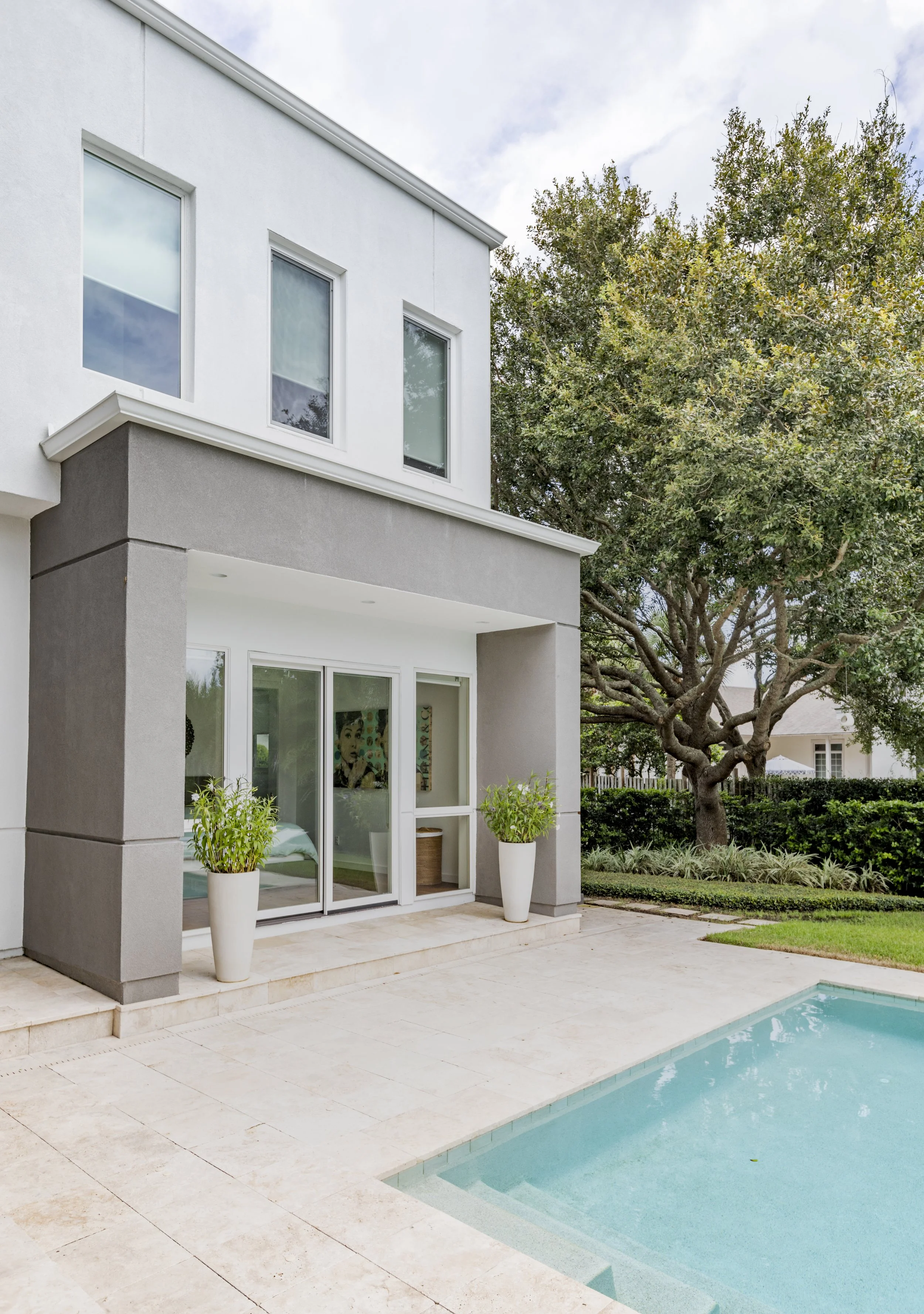 Modern house with large windows, sliding glass doors, and a swimming pool in the backyard, surrounded by trees and landscaping.