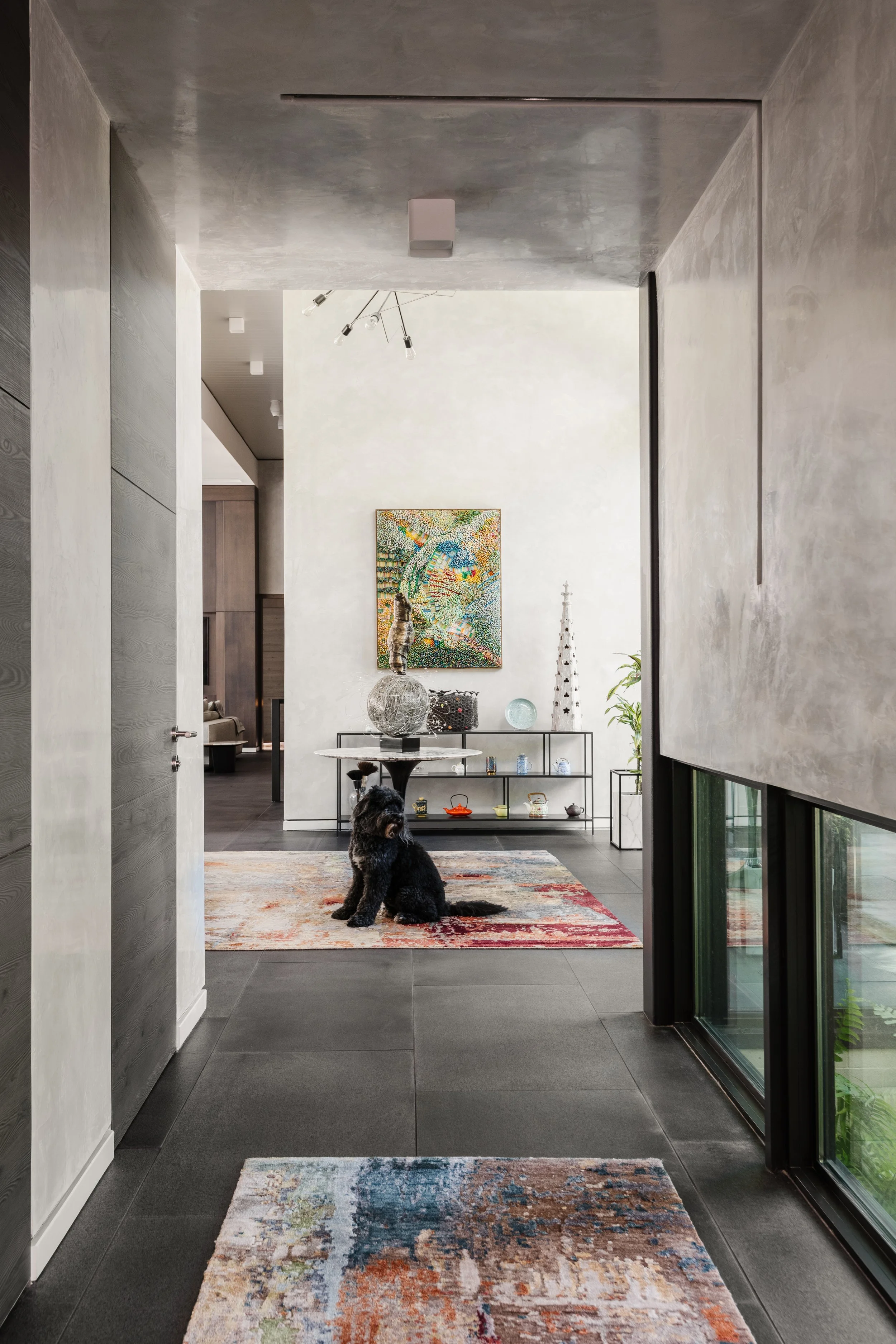 Modern interior hallway leading into a living space with artwork on the wall and a black dog sitting on a multicolored rug.