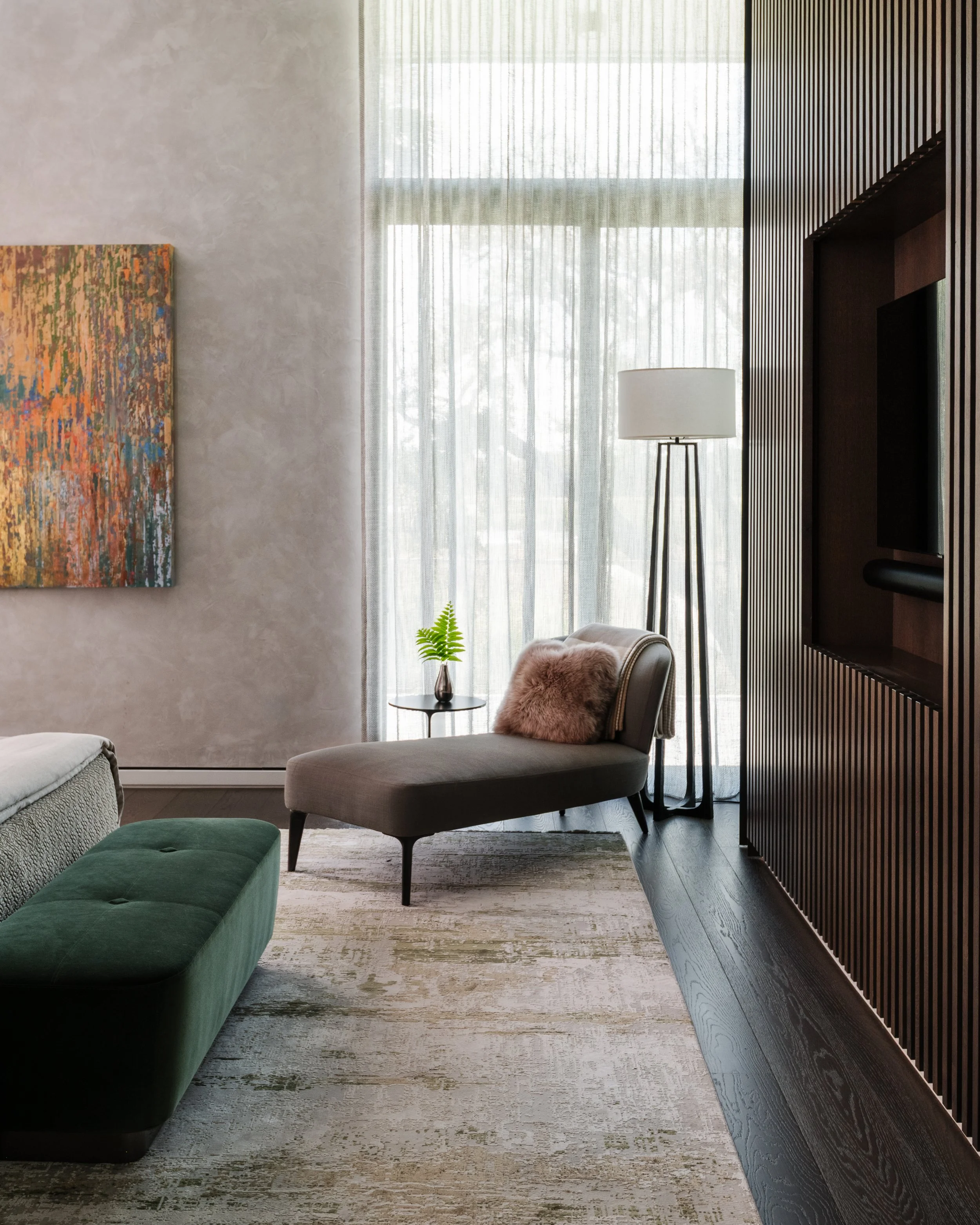 Modern living room with a green sofa, a gray armchair with a pink pillow, a black side table with a potted plant, a tall white floor lamp, sheer curtains, and a textured wall with an abstract painting.