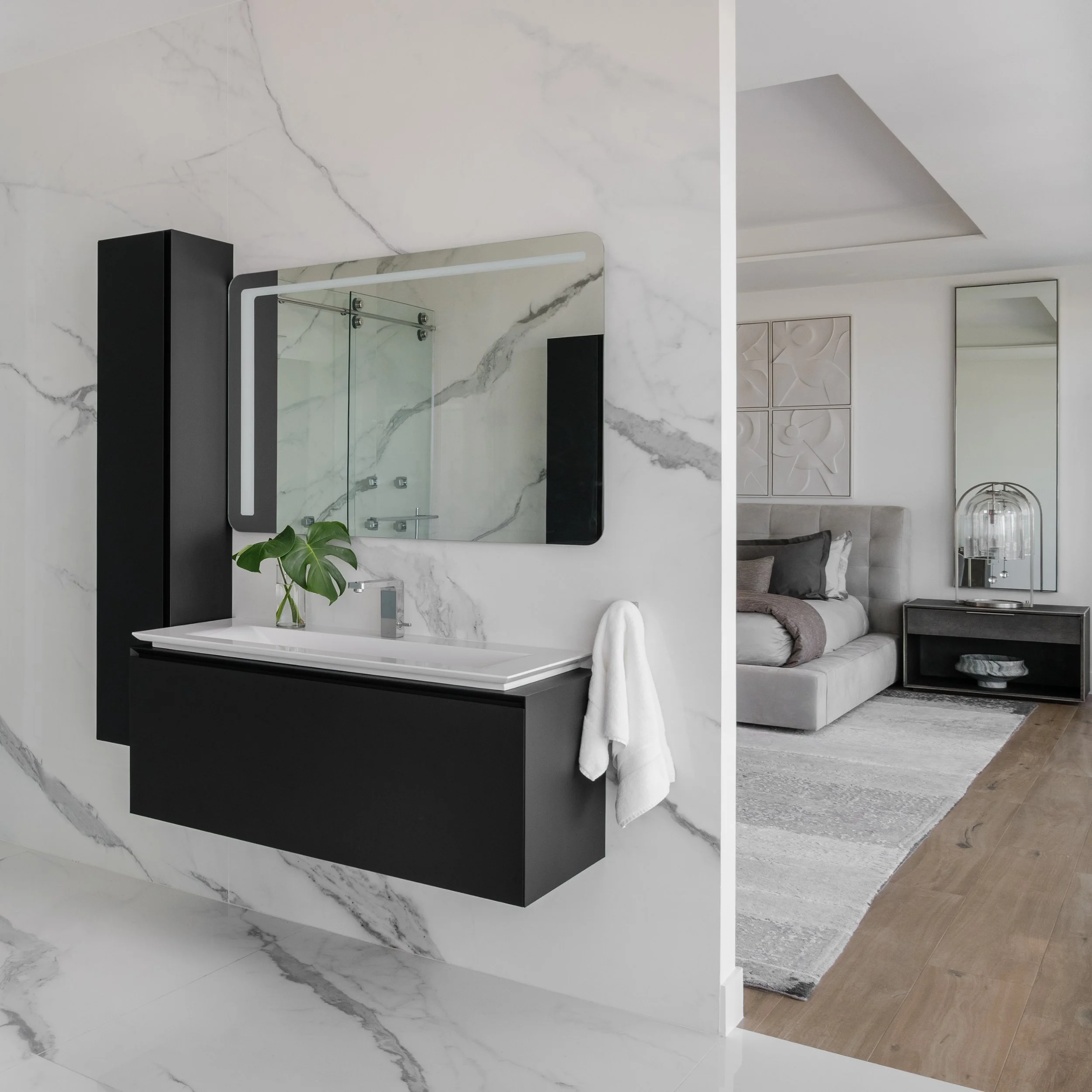 Modern interior space featuring marble walls, a mirror, a black and white vanity, and a background area with a TV and artwork.