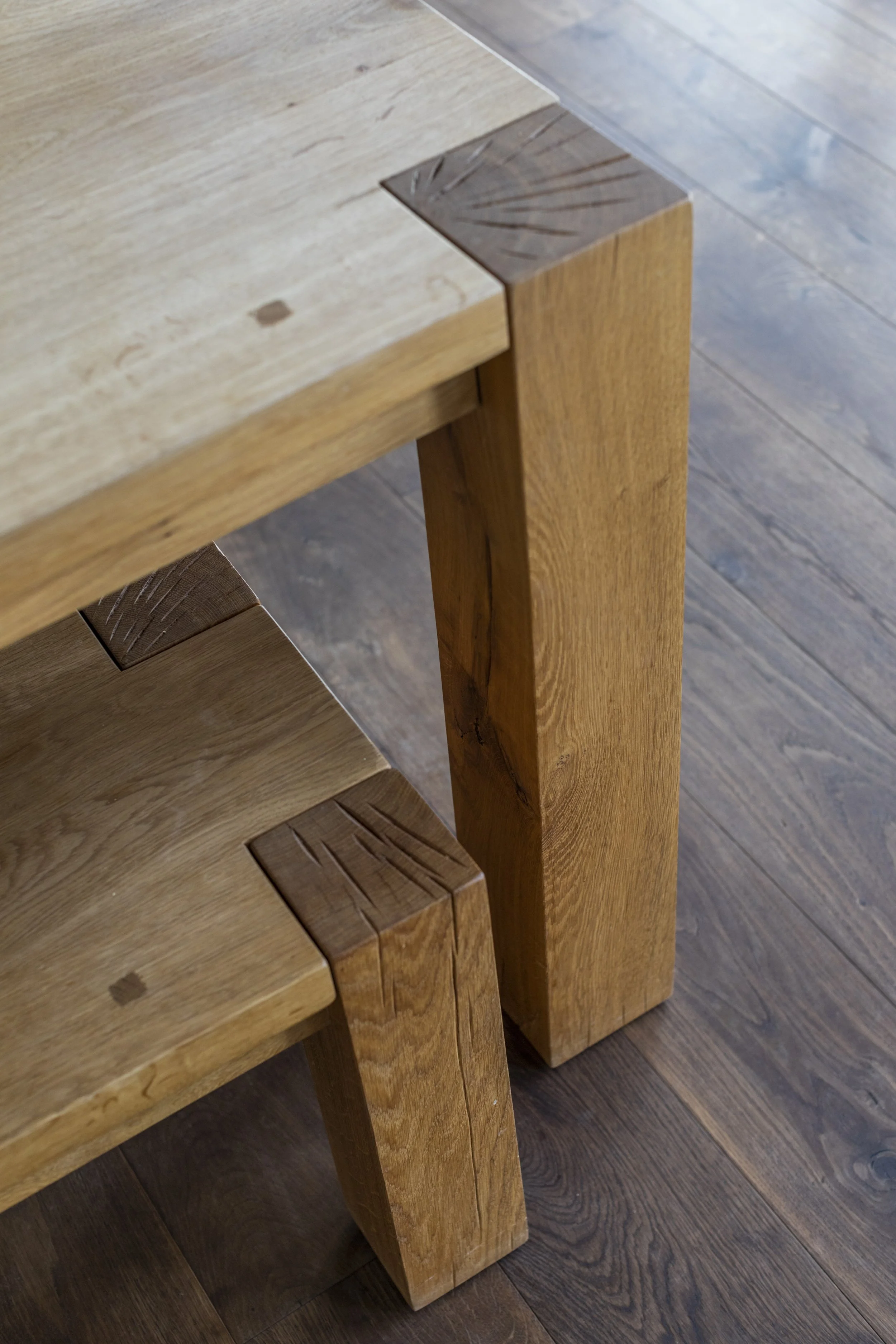 Close-up view of a wooden table corner, showing the textured surface and intact grain, with a matching wooden leg on a dark hardwood floor.