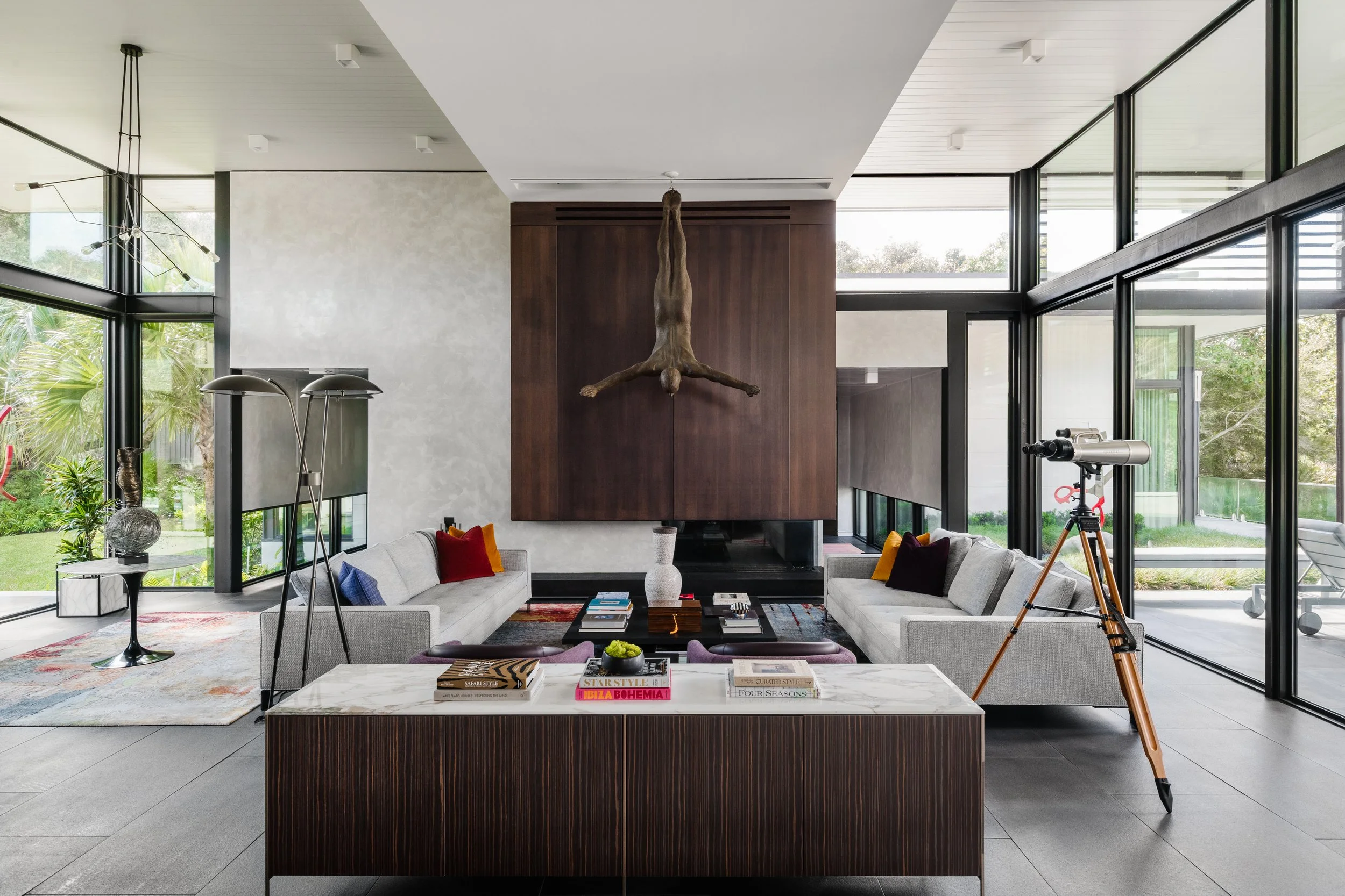 Modern living room with large floor-to-ceiling windows, featuring a spiral staircase, artwork, and a telescope.