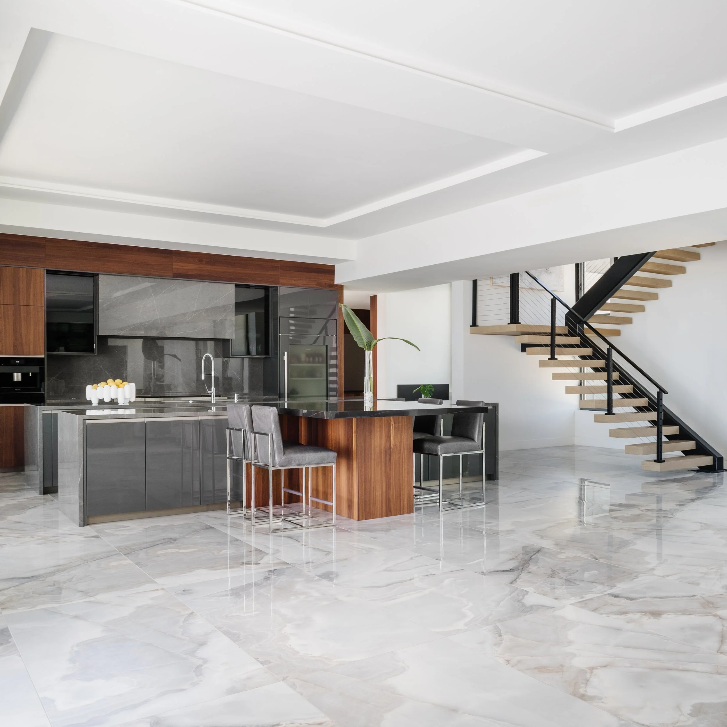 Modern kitchen with marble flooring, dark wood cabinets, a black countertop, and a staircase with wooden steps and black railing.